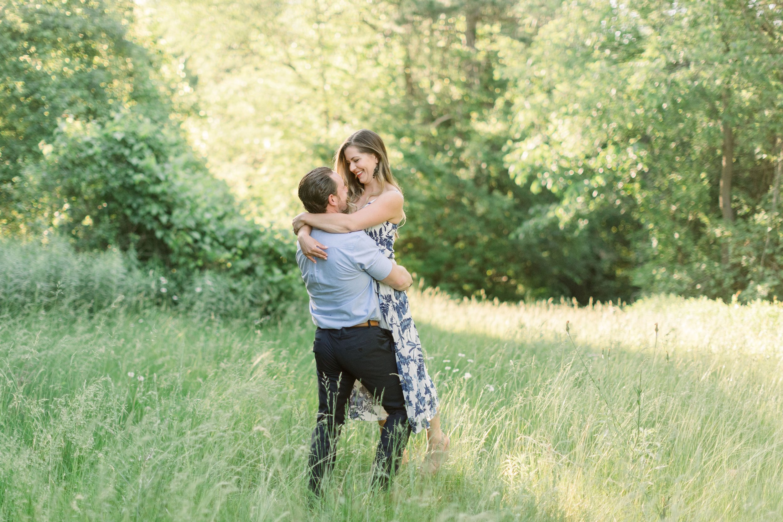  In a field of green grass, an engaged couple hugs with golden sunlight behind them by Chelsea Mason Photography. summer engagements #chelseamasonphotography #chelseamasonengagements #OttawaEngagements #Almonteengagementphotographer #outdoorengagment
