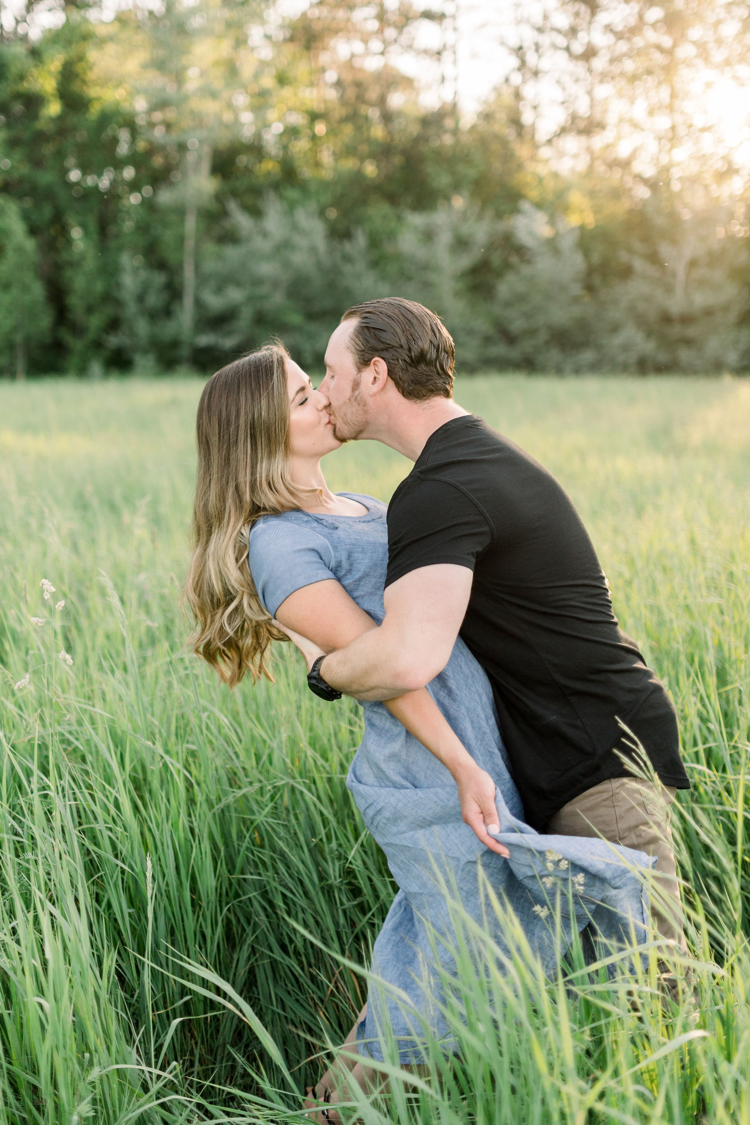  Engaged couple kiss in a green grass clearing in Almonte by Chelsea Mason Photography. mountain engagements in summer black shirt #chelseamasonphotography #chelseamasonengagements #Ottawaengagments #Almonteengagementphotographer #outdoorengagments 