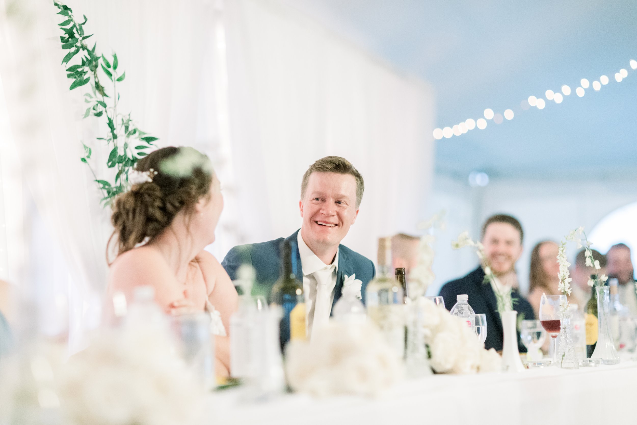  Chelsea Mason Photography captures a groom laughing with the bride sitting at the luncheon head table. groom laughing wedding luncheon #chelseamasonphotography #chelseamasonweddings #Ontarioweddings #Boulterweddingphotographer #laceweddinggown 
