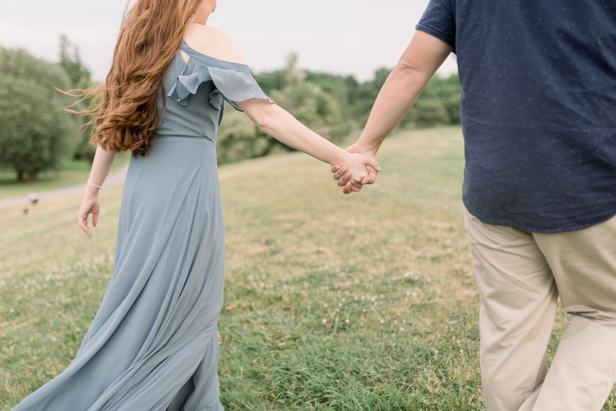  Detailed engagement picture of a man and woman holding hands in a grass field by Chelsea Mason Photography. outdoor wedding announcement pic #chelseamasonphotography #chelseamasonengagements #Ottawaengagements #DominonArboretum #Ottawaphotographers&