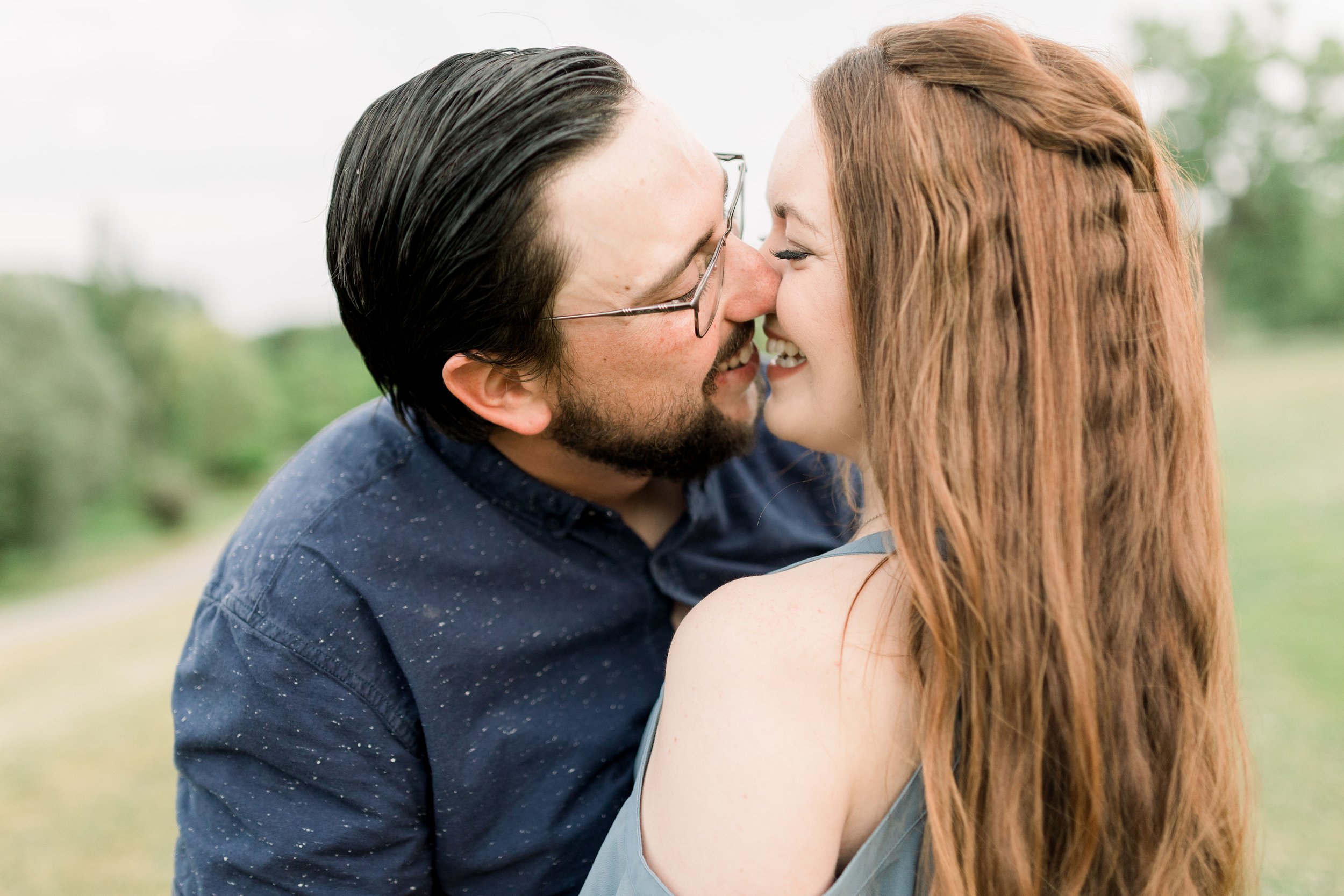  In Ottawa, an engaged couple kisses as the woman laughs by Chelsea Mason Photography. red boho engagement hair kissing couple blue button-up #chelseamasonphotography #chelseamasonengagements #Ottawaengagements #DominonArboretum #Ottawaphotographers&