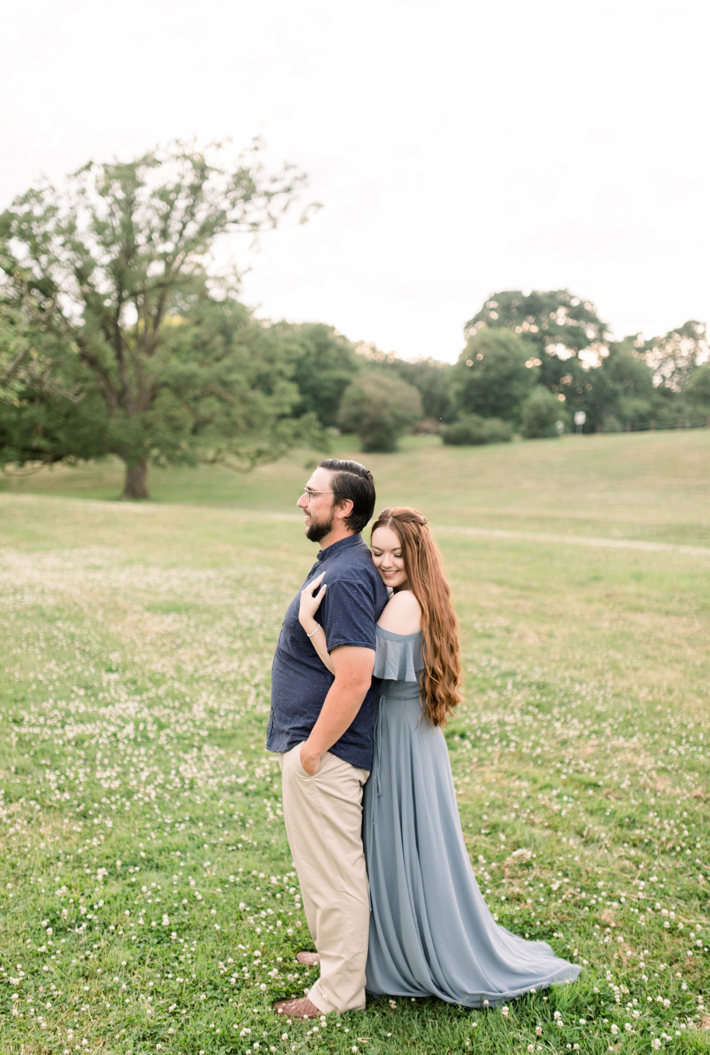  A woman with long red hair holds onto her fiance in a grass field during engagements with Chelsea Mason Photography. fairytale engagements #chelseamasonphotography #chelseamasonengagements #Ottawaengagements #DominonArboretum #OttawaPhotographers&nb