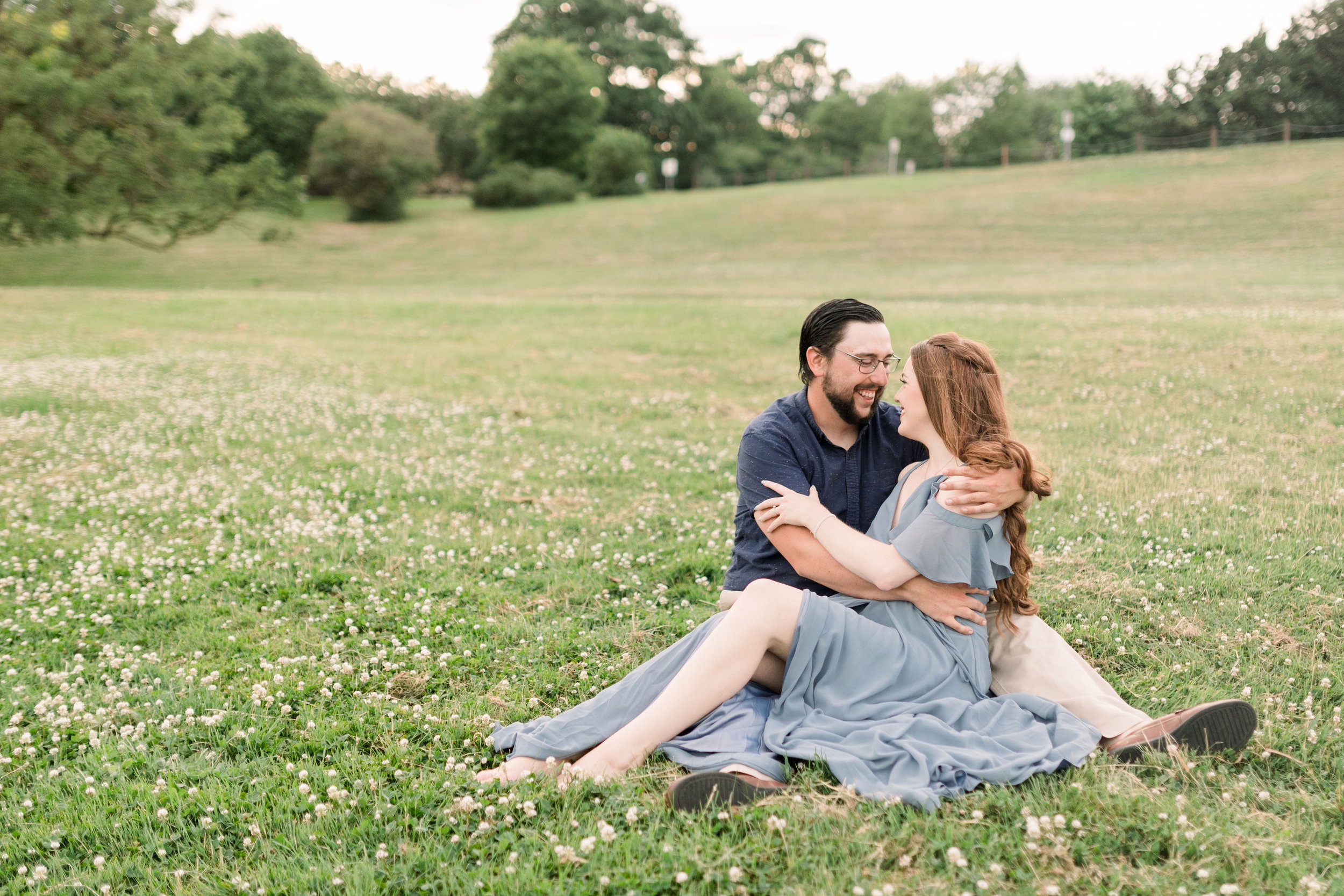  In a green field with white flowers, an engaged couple sits together by Chelsea Mason Photography. dreamy engagement portraits #chelseamasonphotography #chelseamasonengagements #Ottawaengagements #DominonArboretum #Ottawaphotographers&nbsp; 