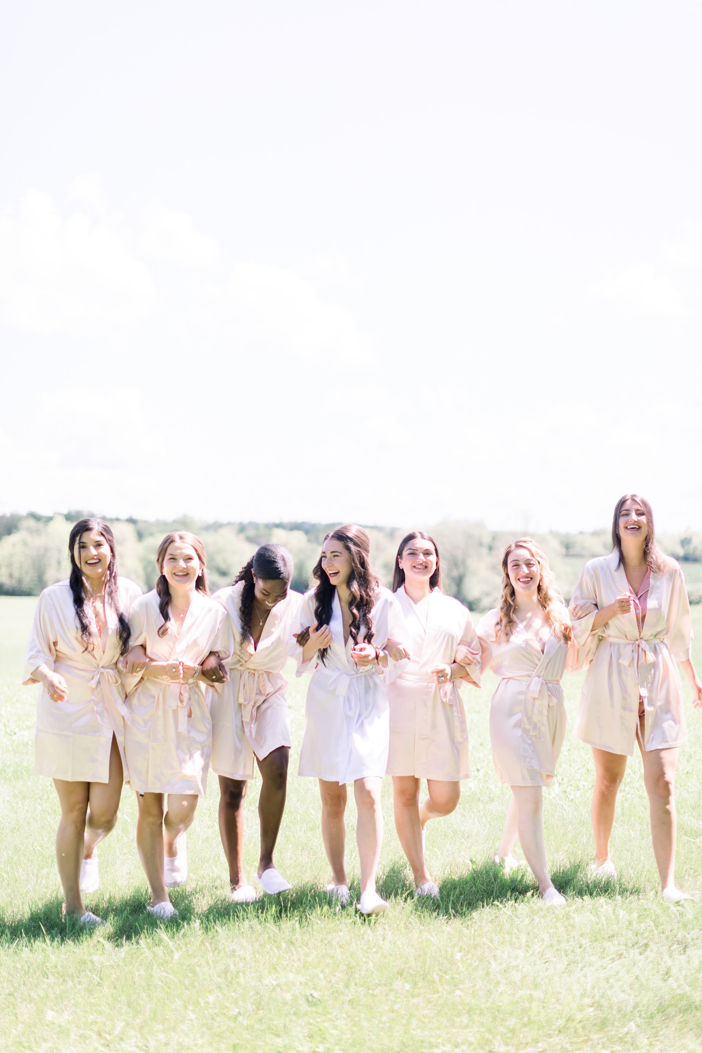  A bride with her bridesmaids walks with linked arms in robes by Chelsea Mason Photography in Ontario. bridesmaid robe matching robe #Chelseamasonphotography #Chelseamasonweddings #Onatarioweddings #EvermoreweddingsAlmonte #Ontarioweddingphotographer