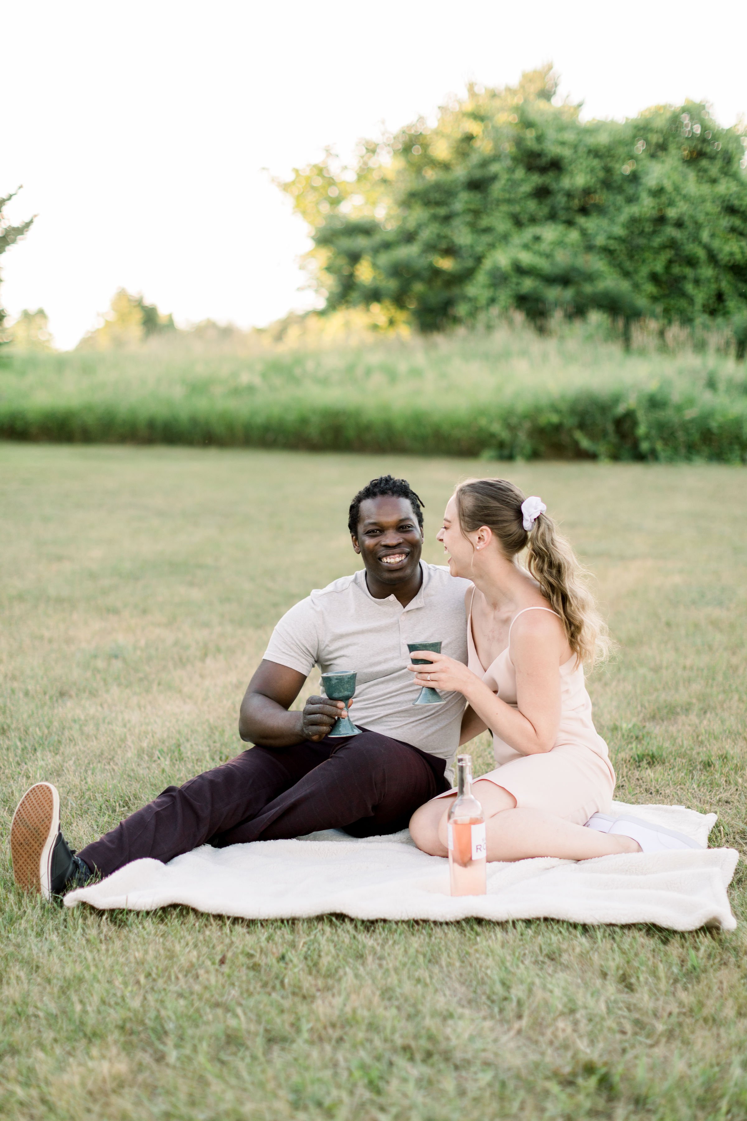  Chelsea Mason Photography captures a couple sitting on a blanket toasting. toasting on a blanket engagements with champagne #Chelseamasonphotography #Chelseamasonengagements #Onatarioengagements #Pinhey'sPoint #Ontarioweddingphotographers 