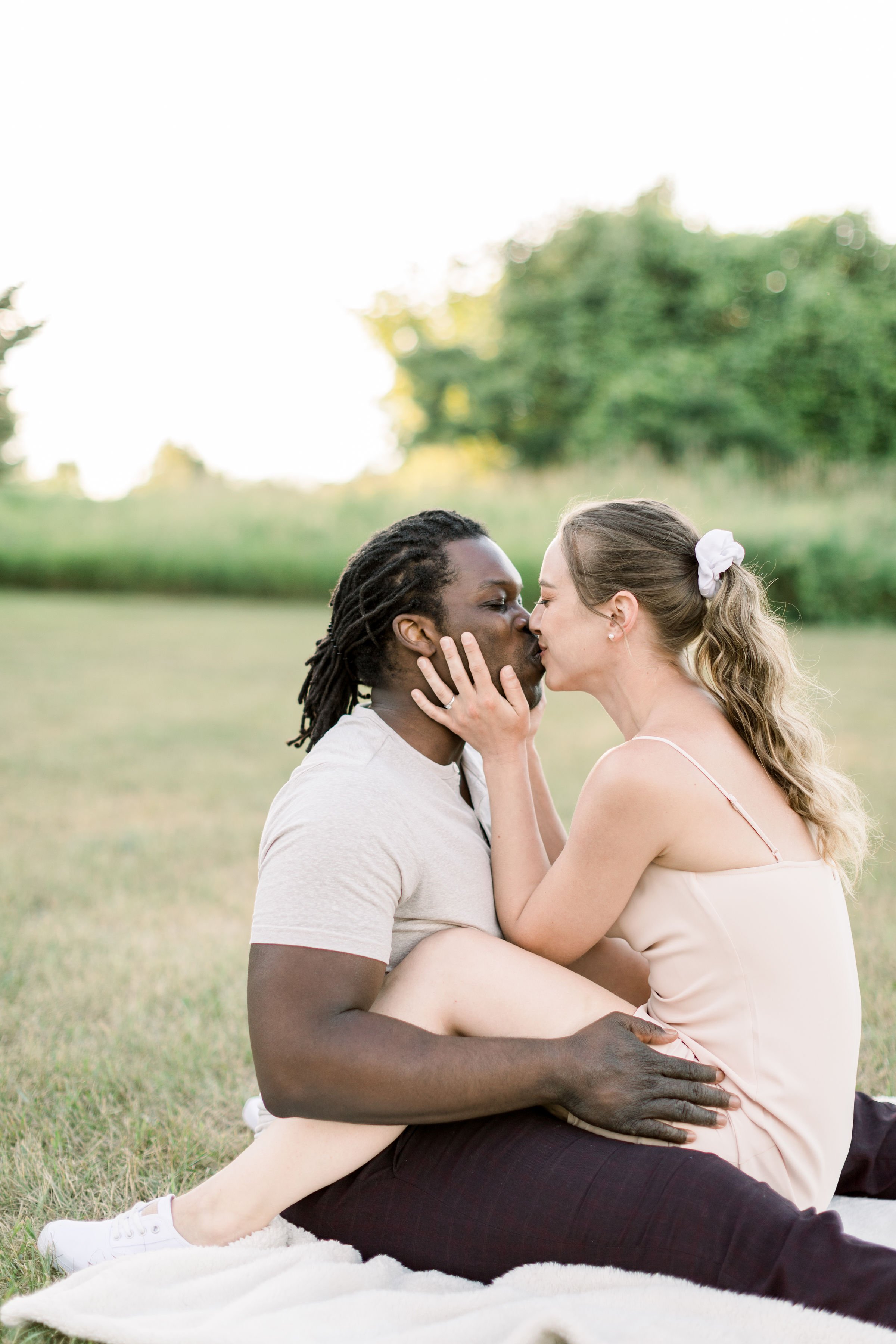  Picnic engagement portraits with a woman kissing a man while sitting on his lap by Chelsea Mason Photography. picnic engagement #Chelseamasonphotography #Chelseamasonengagements #Onatarioengagements #Pinhey'sPoint #Ontarioweddingphotographers 