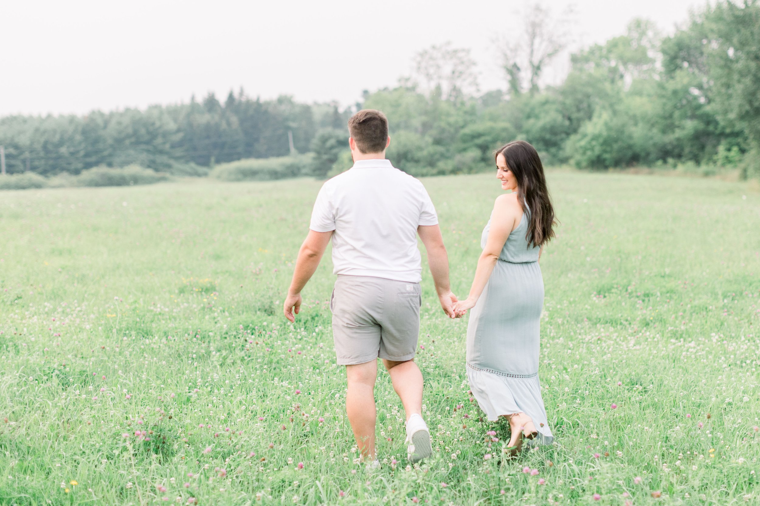  Walking in a field at Grass Creek Park engaged couple holds hands at dusk by Chelsea Mason Photography. summer engagement #Kingstonengagement #GrassCreekParkPortraits #Ontarioengagementphotographers #Chelseamasonphotography #Chelseamasonengagements 