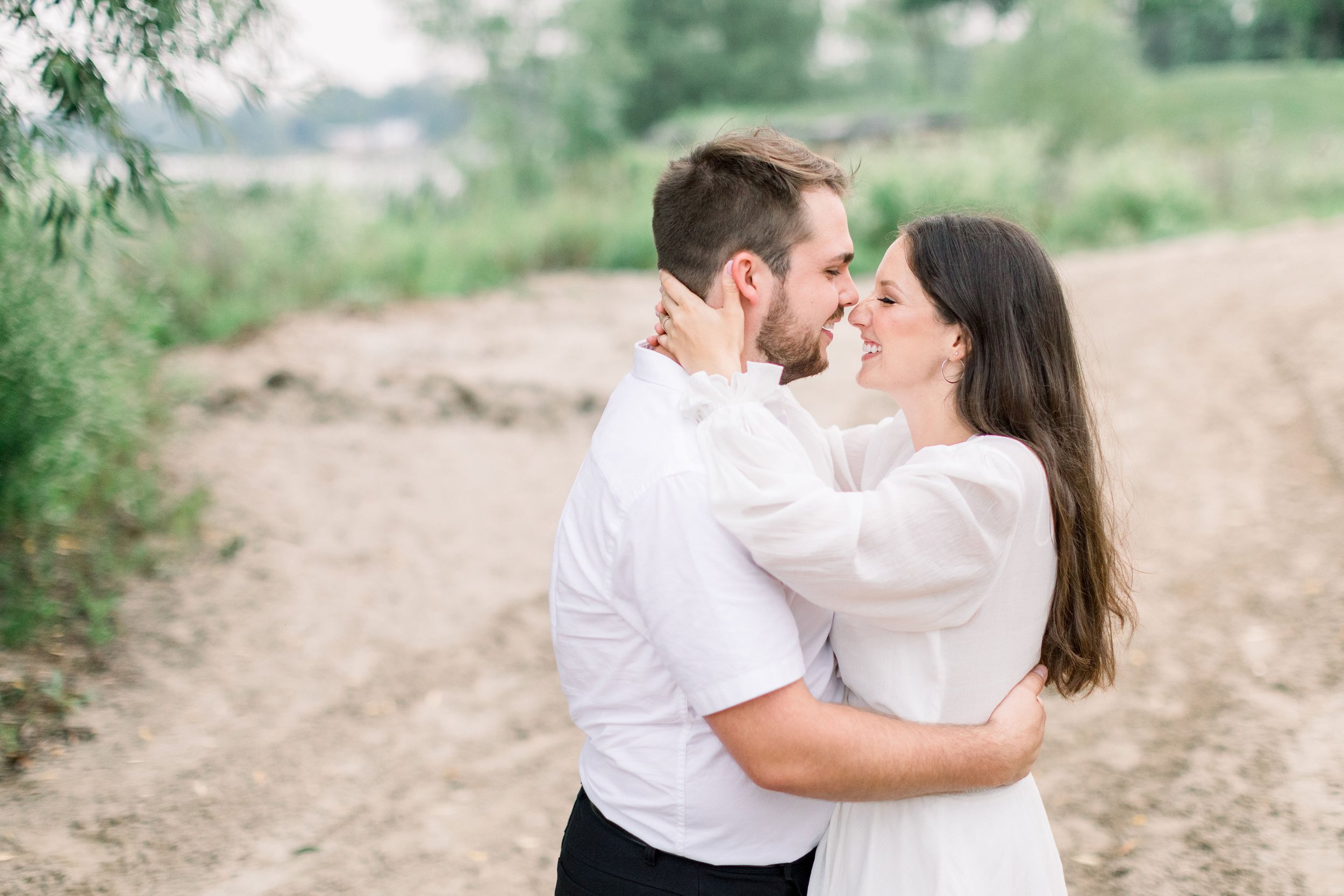  On a dirt path in Kingston Chelsea Mason Photography captures fiances kissing wearing white. white for engagements outdoors #Kingstonengagement #GrassCreekParkPortraits #Ontarioengagementphotographers #Chelseamasonphotography #Chelseamasonengagement