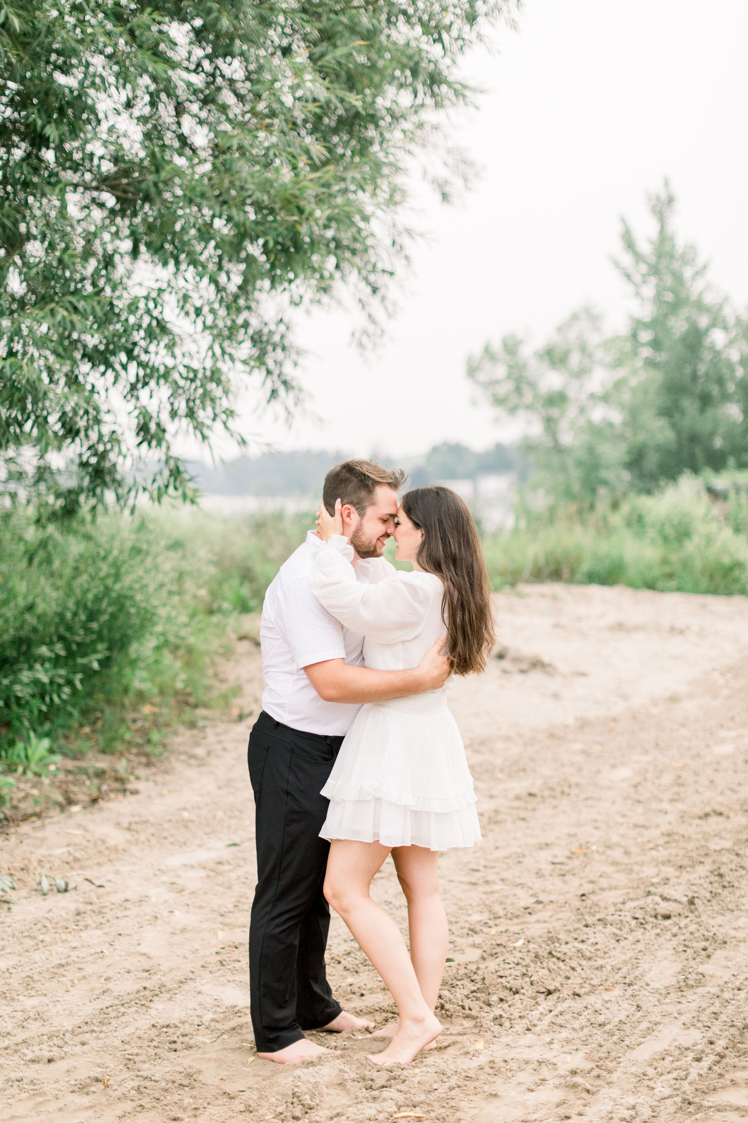  A woman goes in for a kiss during an engagement session with Chelsea Mason Photography. foreheads together leg pop kiss #Kingstonengagement #GrassCreekParkPortraits #Ontarioengagementphotographers #Chelseamasonphotography #Chelseamasonengagements 