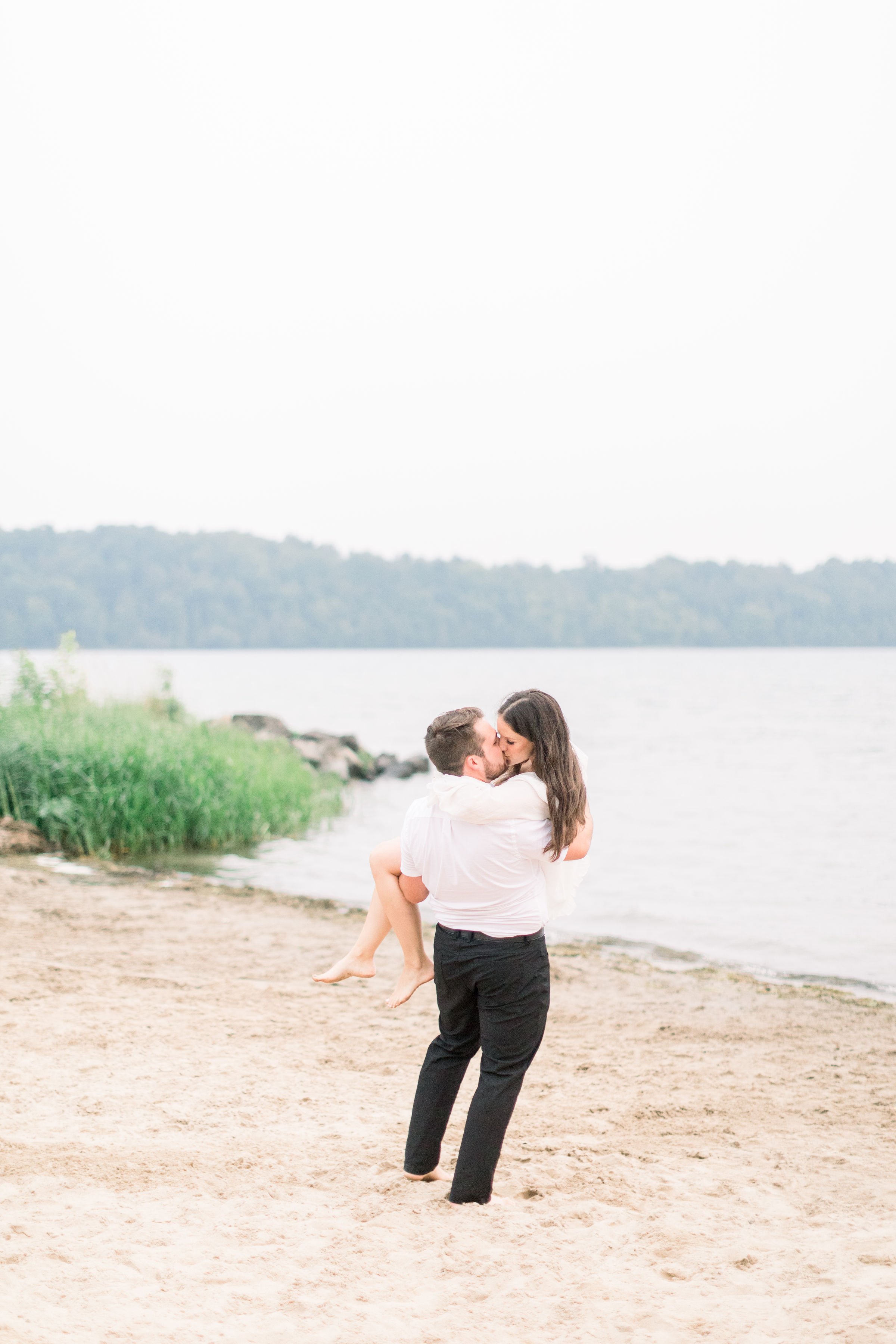  Chelsea Mason Photography captures a man carrying his fiance next to a lake at Grass Creek Park. engagement portraits lake #Kingstonengagement #GrassCreekParkPortraits #Ontarioengagementphotographers #Chelseamasonphotography #Chelseamasonengagements