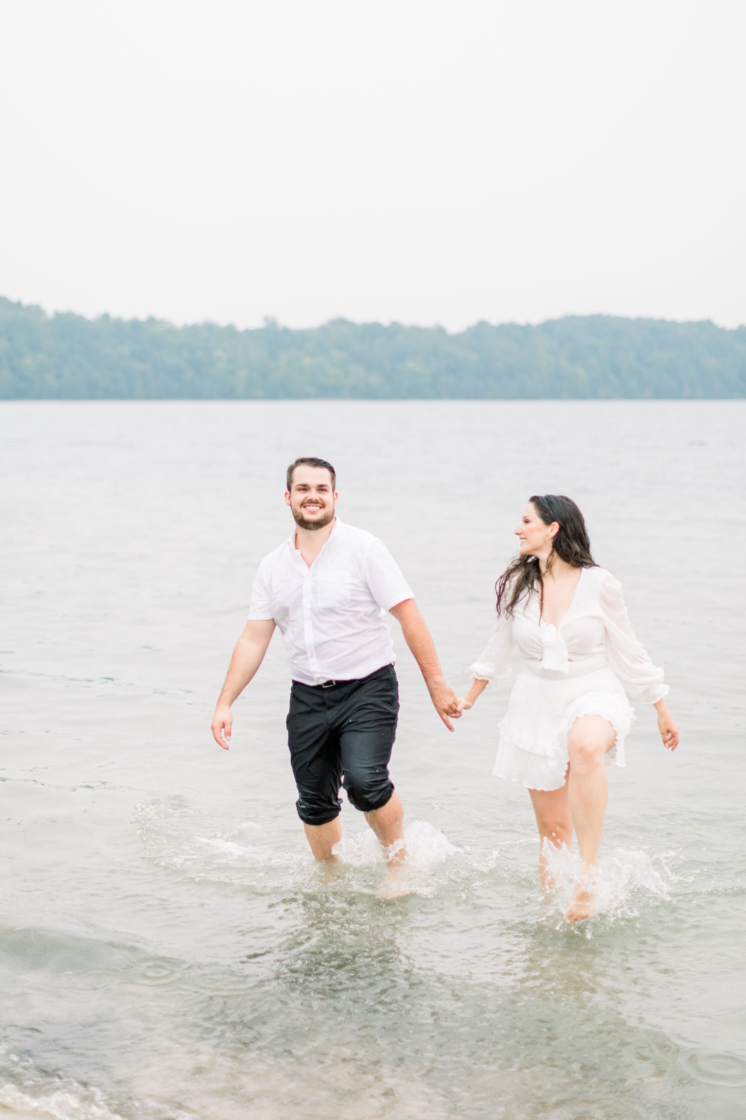  Hand-in-hand engaged couple walk out of the lake together captured by Chelsea Mason Photography. hand in hand lake portrait #Kingstonengagement #GrassCreekParkPortraits #Ontarioengagementphotographers #Chelseamasonphotography #Chelseamasonengagement