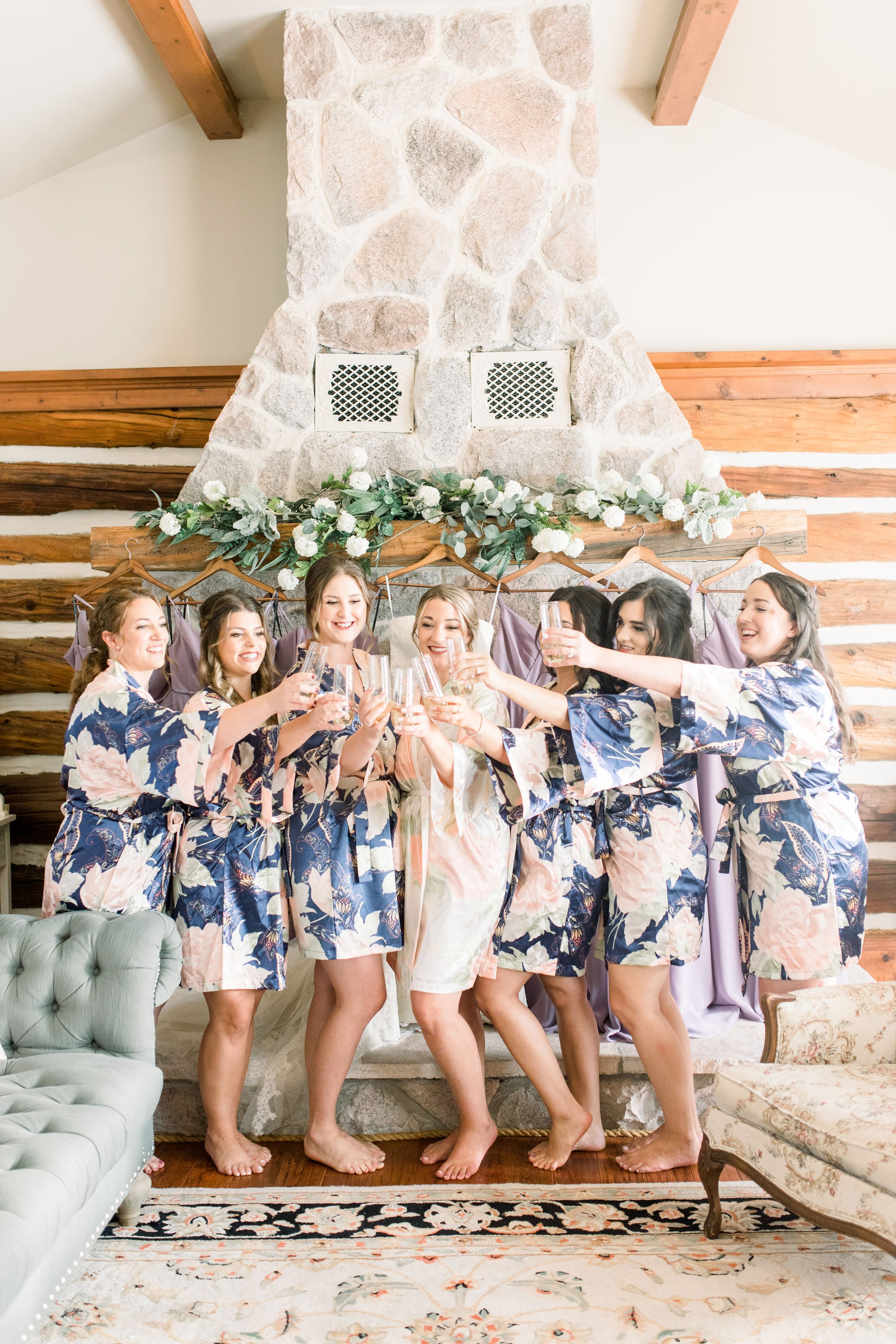  Bridesmaids in front of a stone fireplace in floral robes toasting by Chelsea Mason Photography. floral bridesmaid robe toasting #StonefieldEstates #Ontarioweddings #Chelseamasonphotography #Chelseamasonengagements #Ontarioweddingphotographers 