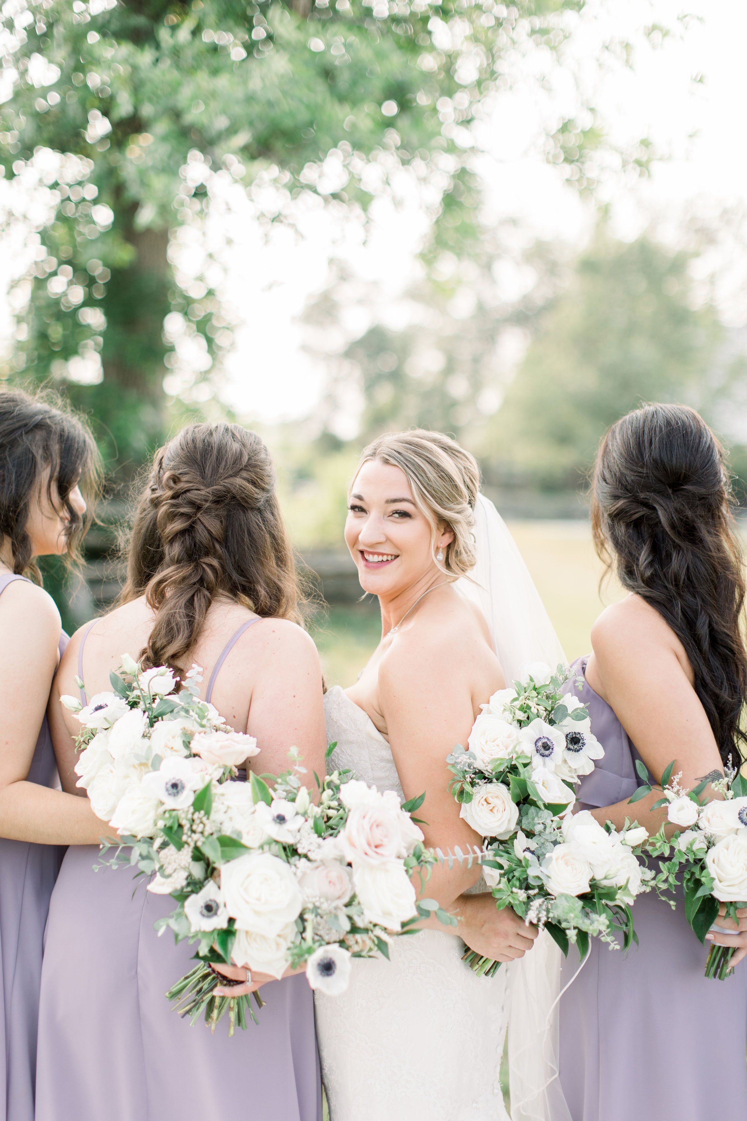  Chelsea Mason Photography captures a bride looking over her shoulder while hugging her bridesmaids. purple bridesmaids dresses #StonefieldEstates #Ontarioweddings #Chelseamasonphotography #Chelseamasonengagements #Ontarioweddingphotographers 