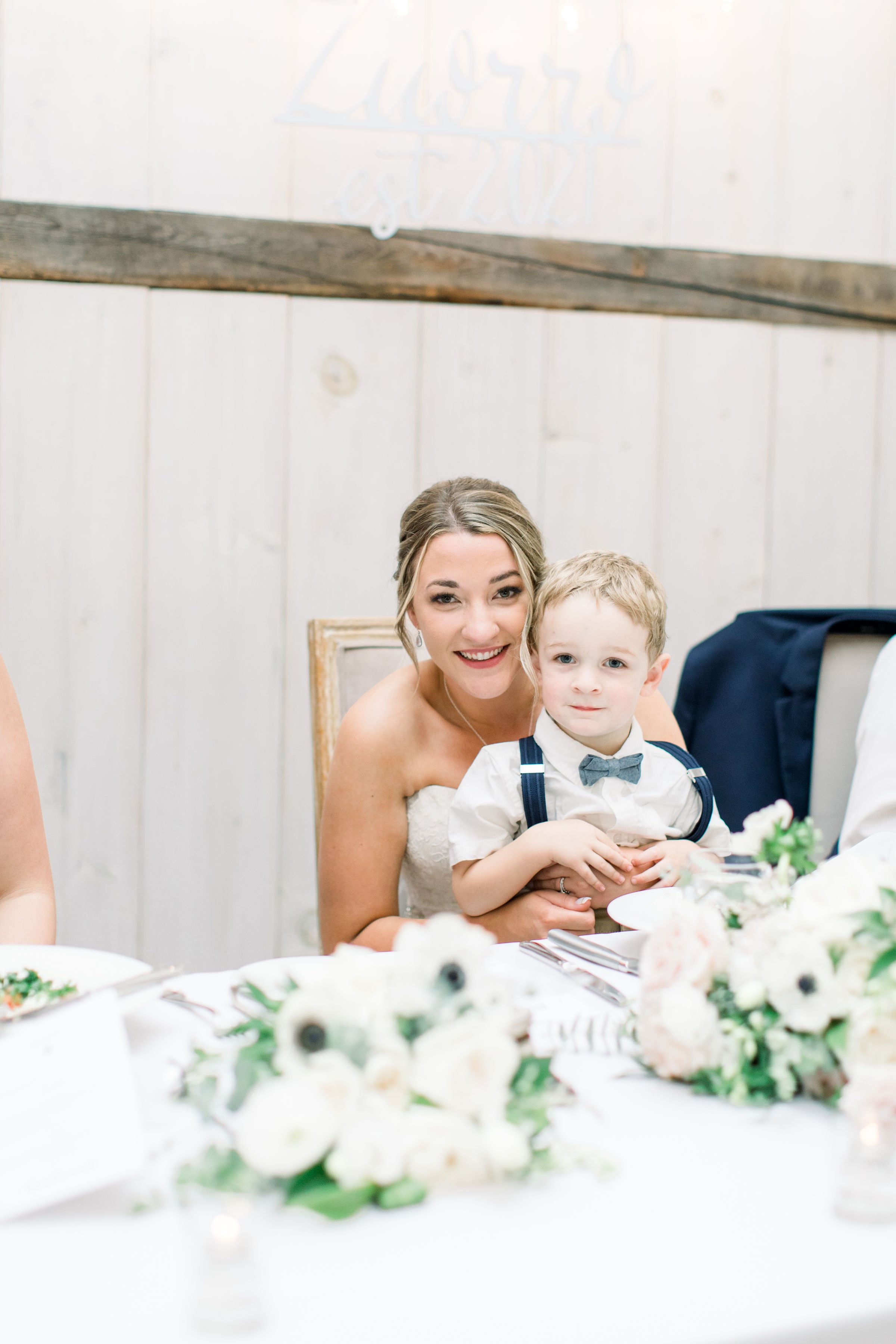  Bride smiles with young ring bearer sitting on her lap by Chelsea Mason Photography. little kids in weddings ring bearer Ontario wed #StonefieldEstates #Ontarioweddings #Chelseamasonphotography #Chelseamasonengagements #Ontarioweddingphotographers 