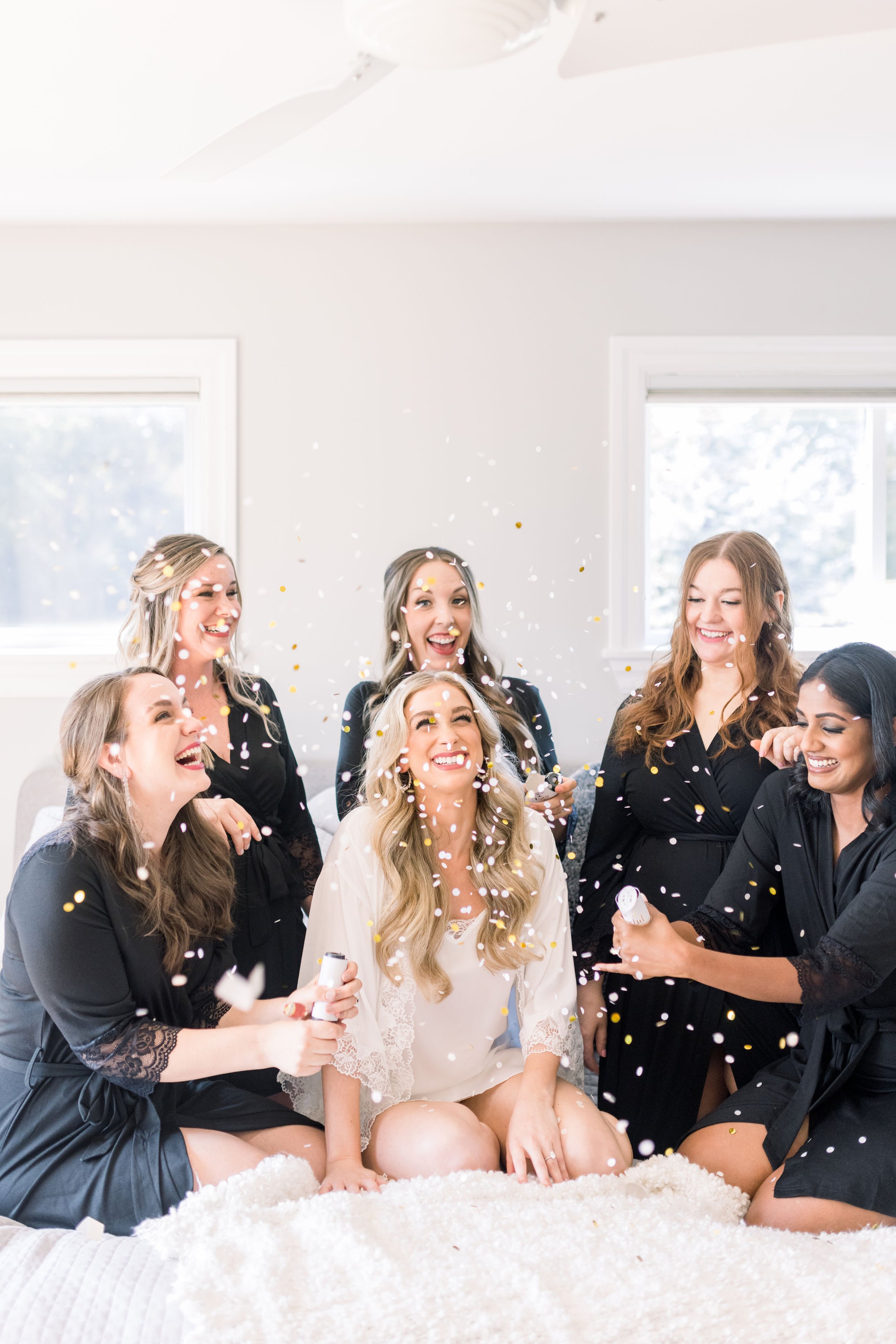  Bride in a white robe sitting on a bed with her bridesmaids was captured by Chelsea Mason Photography. bride getting ready pics #ChelseaMasonPhotography #ChelseaMasonWeddings #PrinceEdwardsCountyWeddings #SandbanksWeddings #ONweddingphotographer 