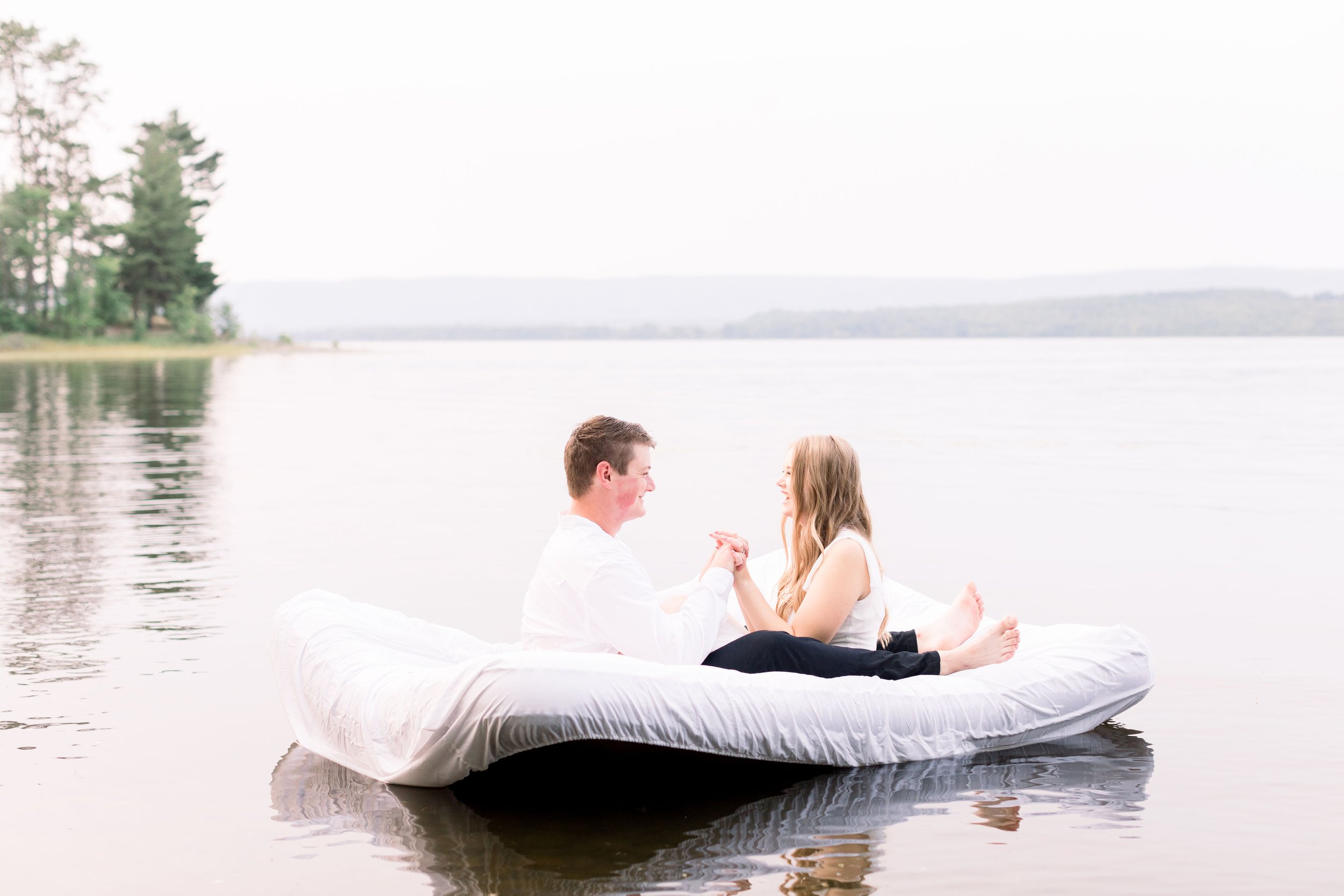  At Pinhey's Point, an engaged couple sits on a mattress on the lake by Chelsea Mason photography. Pinhey's Point engagements Ottawa #ChelseaMasonPhotography #ChelseaMasonEngagements #PinheysPointEngagements #OttawaEngagementPhotography 
