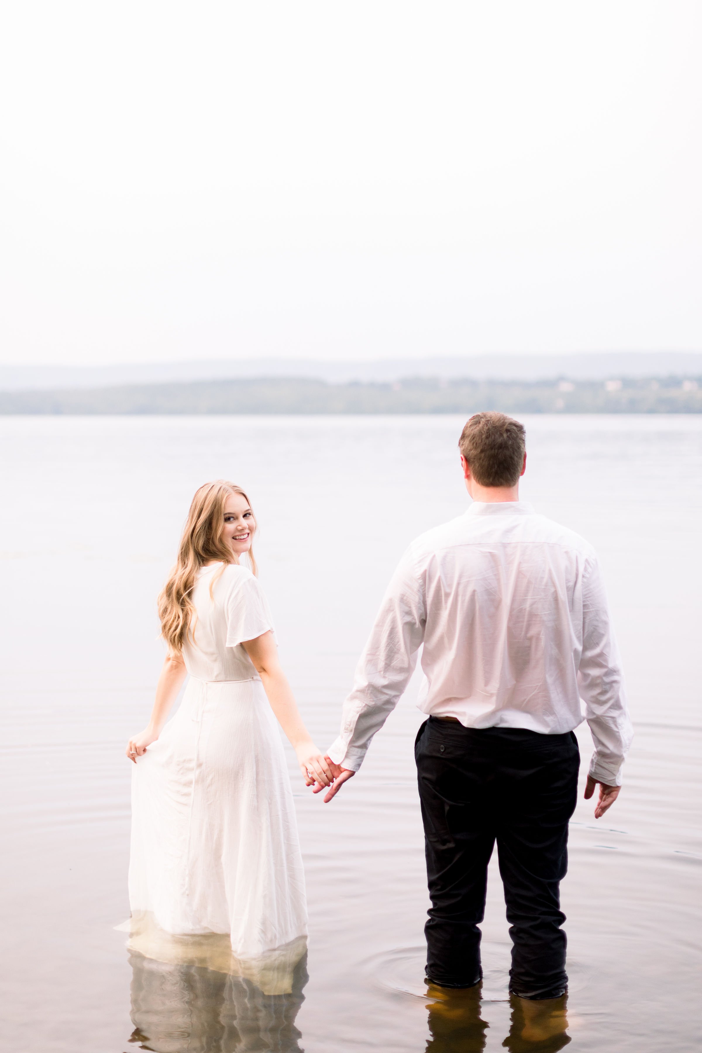  A woman looks over her shoulder while holding hands with her fiance in a lake by Chelsea Mason Photography. fiances she said yes lake pics #ChelseaMasonPhotography #ChelseaMasonEngagements #PinheysPointEngagements #OttawaEngagementPhotography 