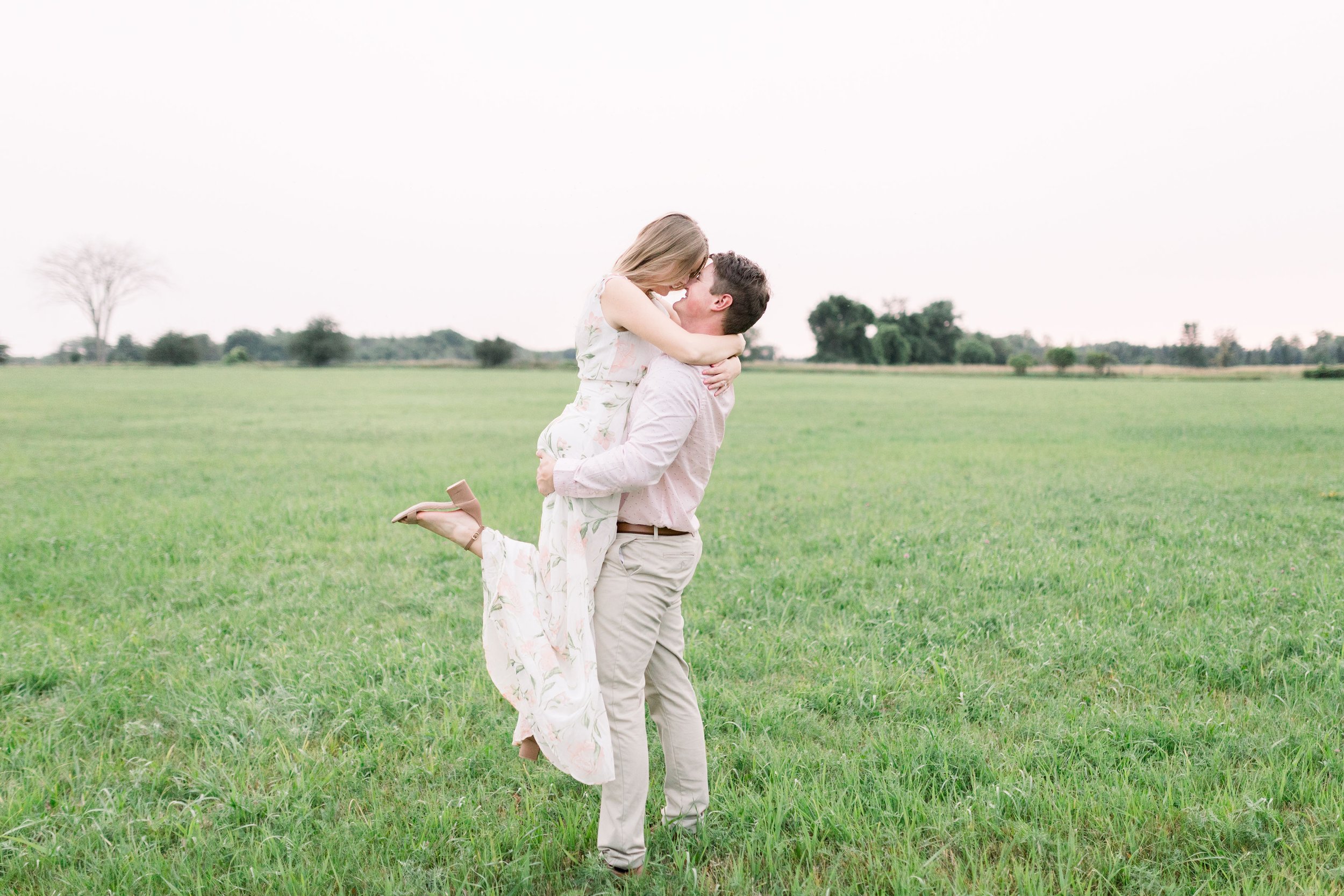  In a grassy field in Ottawa, a man holds a woman in his arm by Chelsea Mason Photography. outside engagements Pinhey's Point Photography #ChelseaMasonPhotography #ChelseaMasonEngagements #PinheysPointEngagements #OttawaEngagementPhotography 