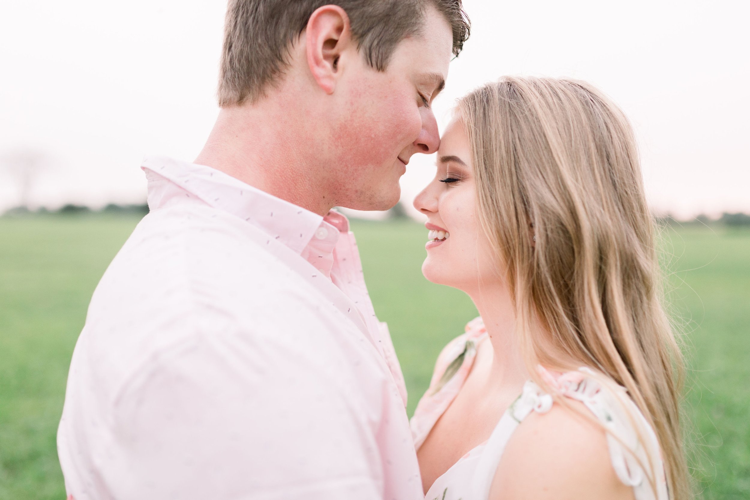  In a pink button-up shirt, a man goes in for a kiss by Chelsea Mason Photography. photographer grass field detailed couple shots Spring outfits #ChelseaMasonPhotography #ChelseaMasonEngagements #PinheysPointEngagements #OttawaEngagementPhotography 