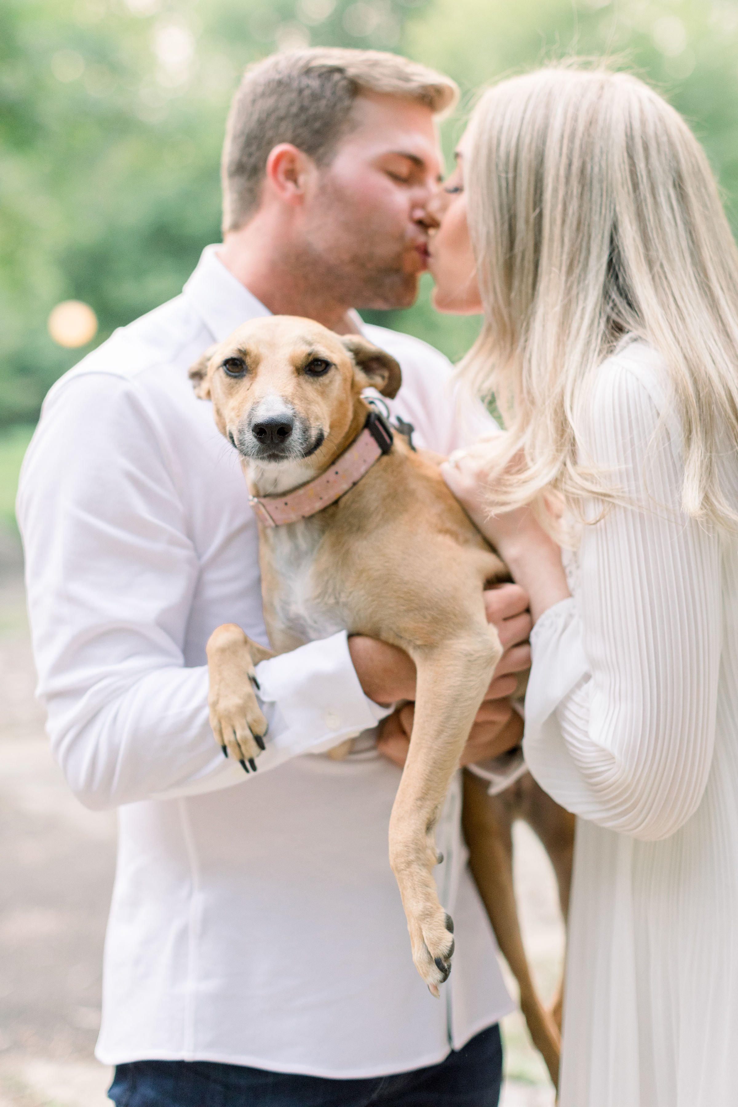  Man and woman kiss while holding their dog in Ottawa by Chelsea Mason Photography. all white engagement outfits center dog #Ottawaengagements #Ottawaweddingphotographers #engagementwithdogs #ChelseaMasonPhotography #ChelseaMasonEngagements  