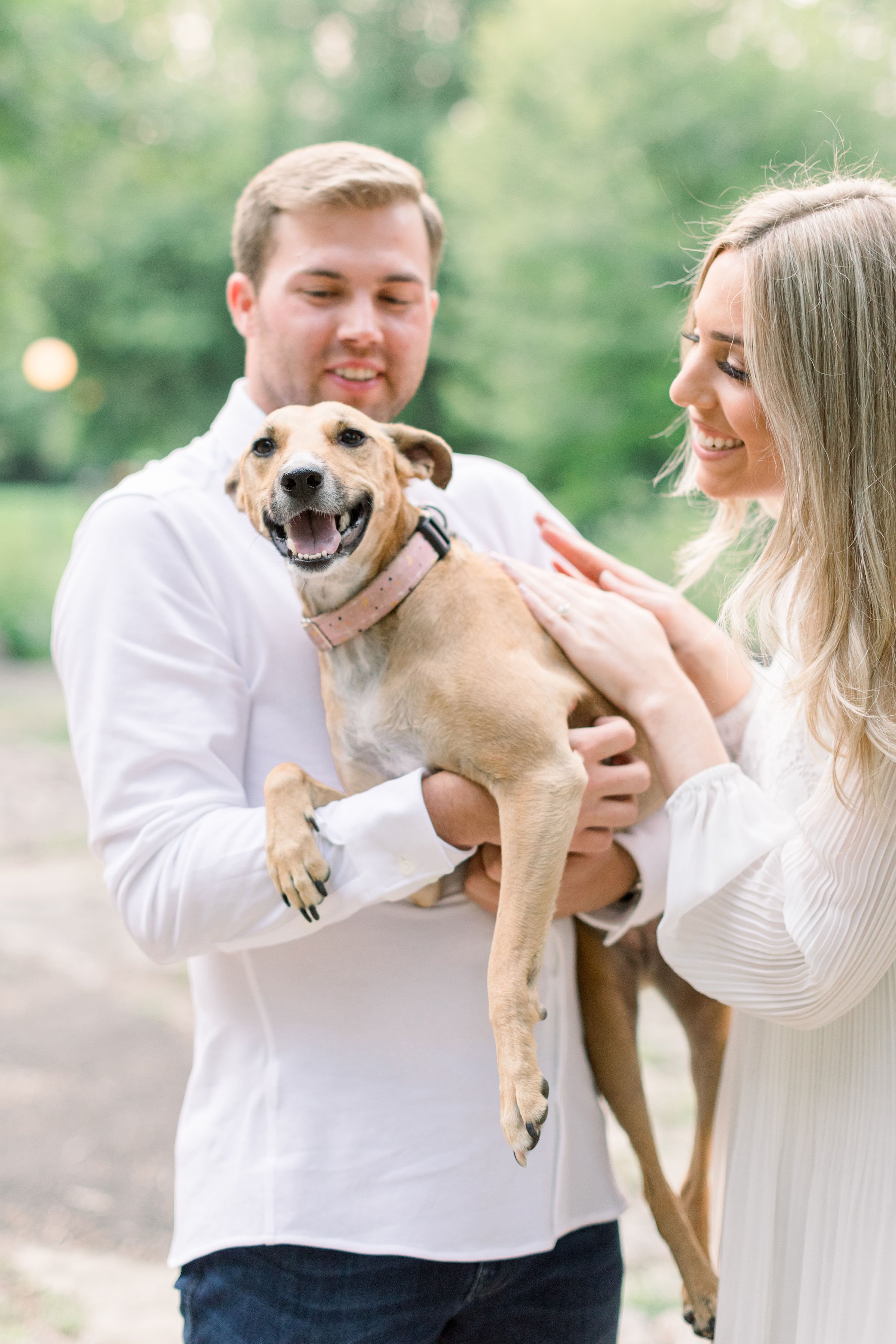  A dog smiles while being held by a man and woman at a park by Chelsea Mason Photography. smiling dog with man and woman Ottawa #Ottawaengagements #Ottawaweddingphotographers #engagementwithdogs #ChelseaMasonPhotography #ChelseaMasonEngagements  