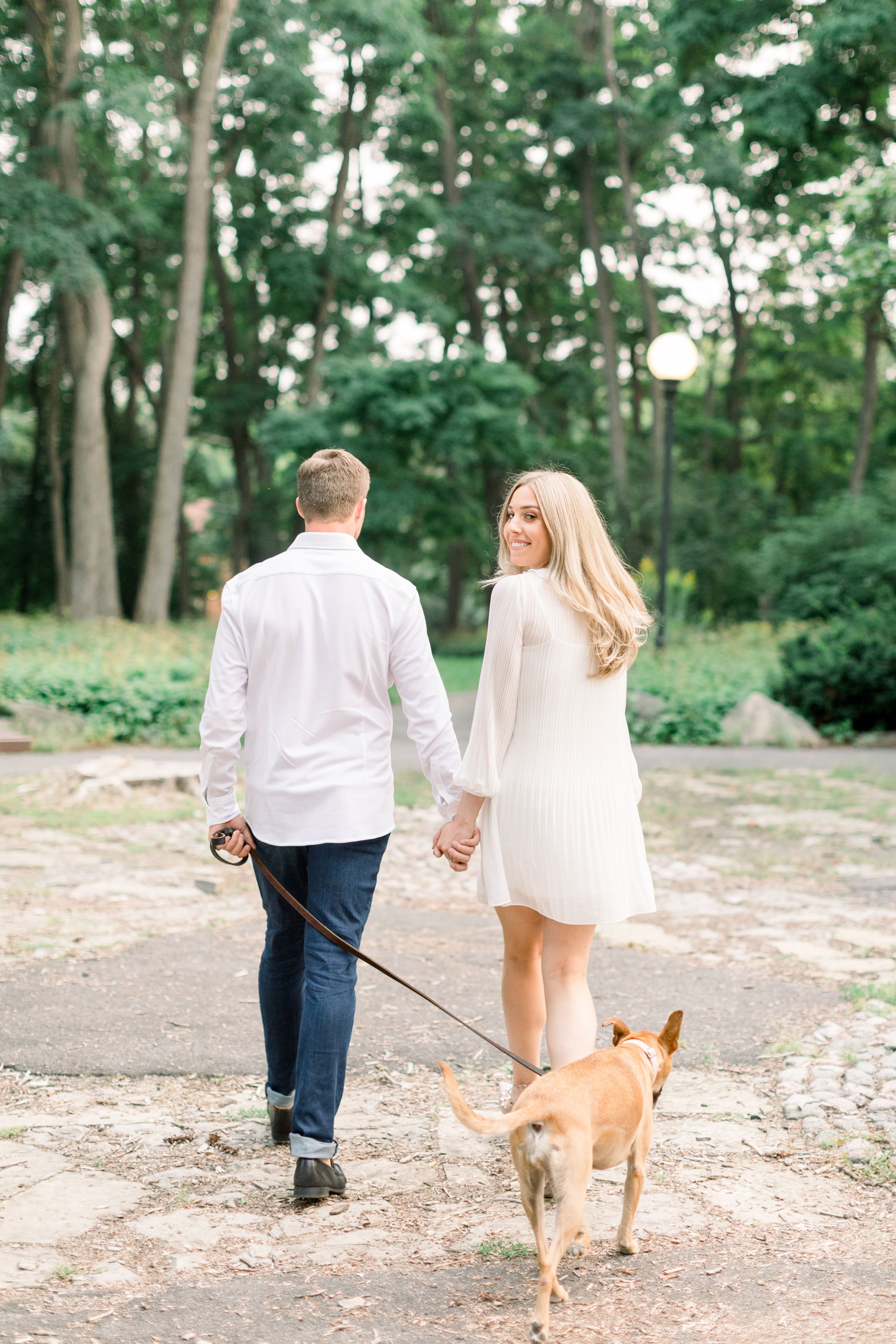  Holding hands with a man a woman looks over her shoulder and smiles by Chelsea Mason Photography. Engaged she said yes authentic #Ottawaengagements #Ottawaweddingphotographers #engagementwithdogs #ChelseaMasonPhotography #ChelseaMasonEngagements  