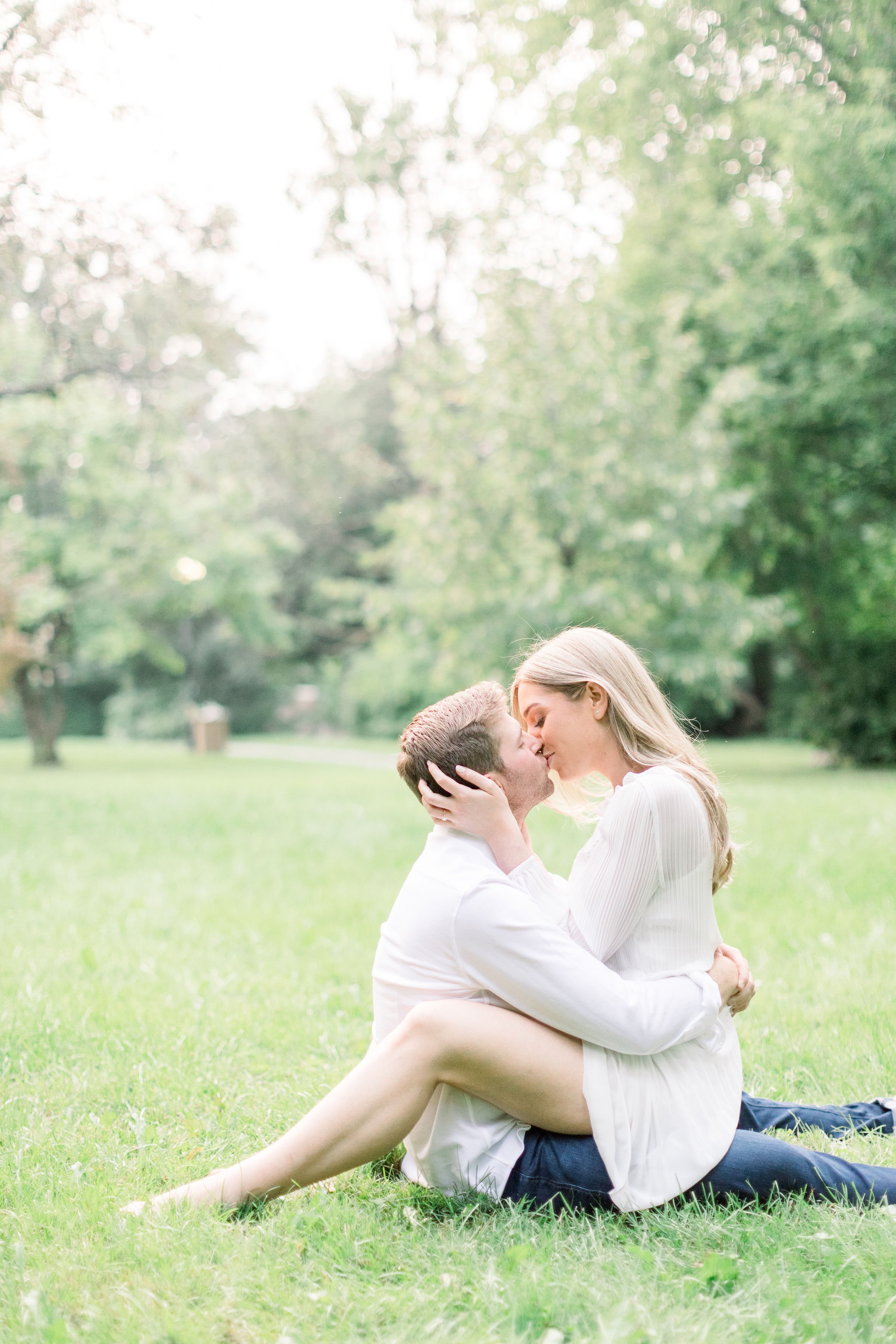  Sitting on a mans lap a woman kisses him holding his head captured by Chelsea Mason Photography. sitting engaged portraits #Ottawaengagements #Ottawaweddingphotographers #engagementwithdogs #ChelseaMasonPhotography #ChelseaMasonEngagements  