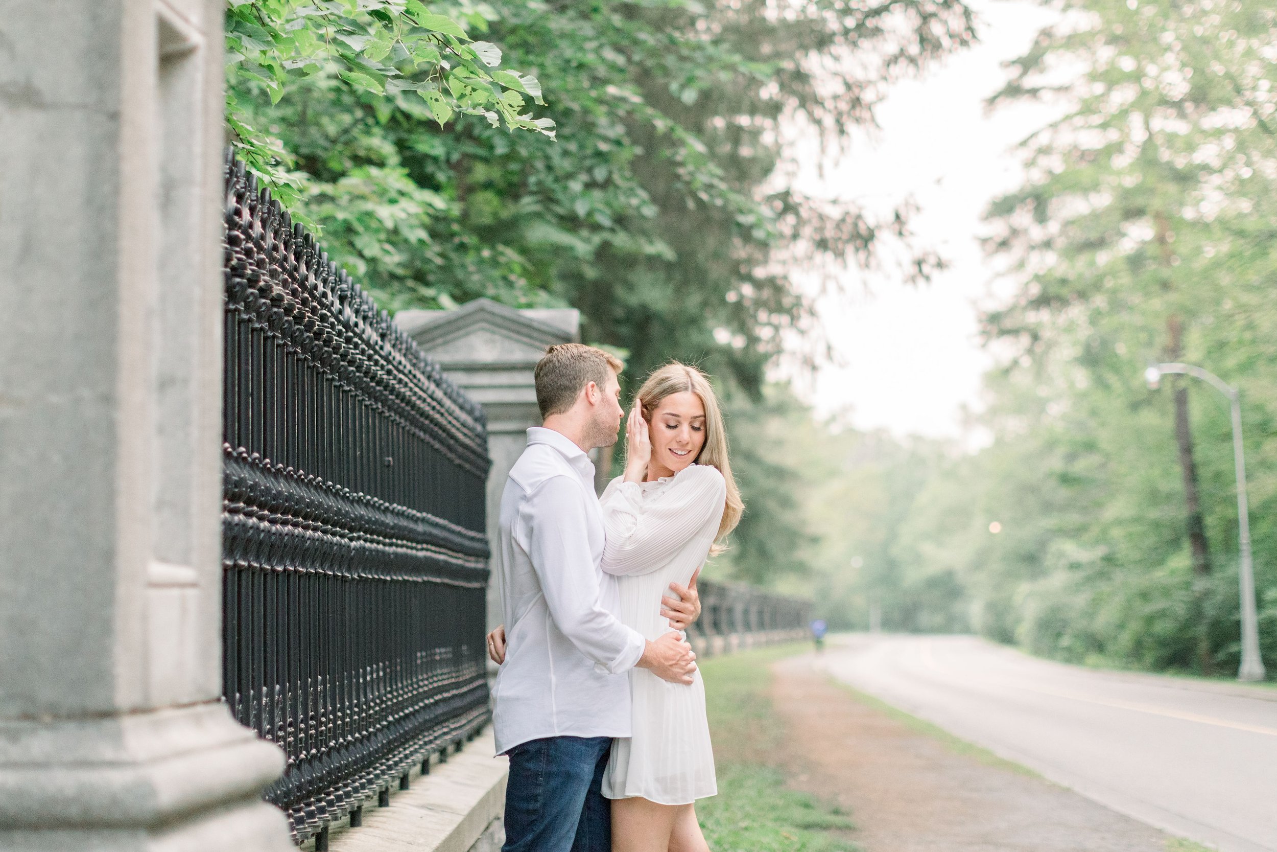  Standing next to a black fence and road a woman tucks her hair behind her ear captured by Chelsea Mason Photography. stunning engagements #Ottawaengagements #Ottawaweddingphotographers #engagement #ChelseaMasonPhotography #ChelseaMasonEngagements&nb