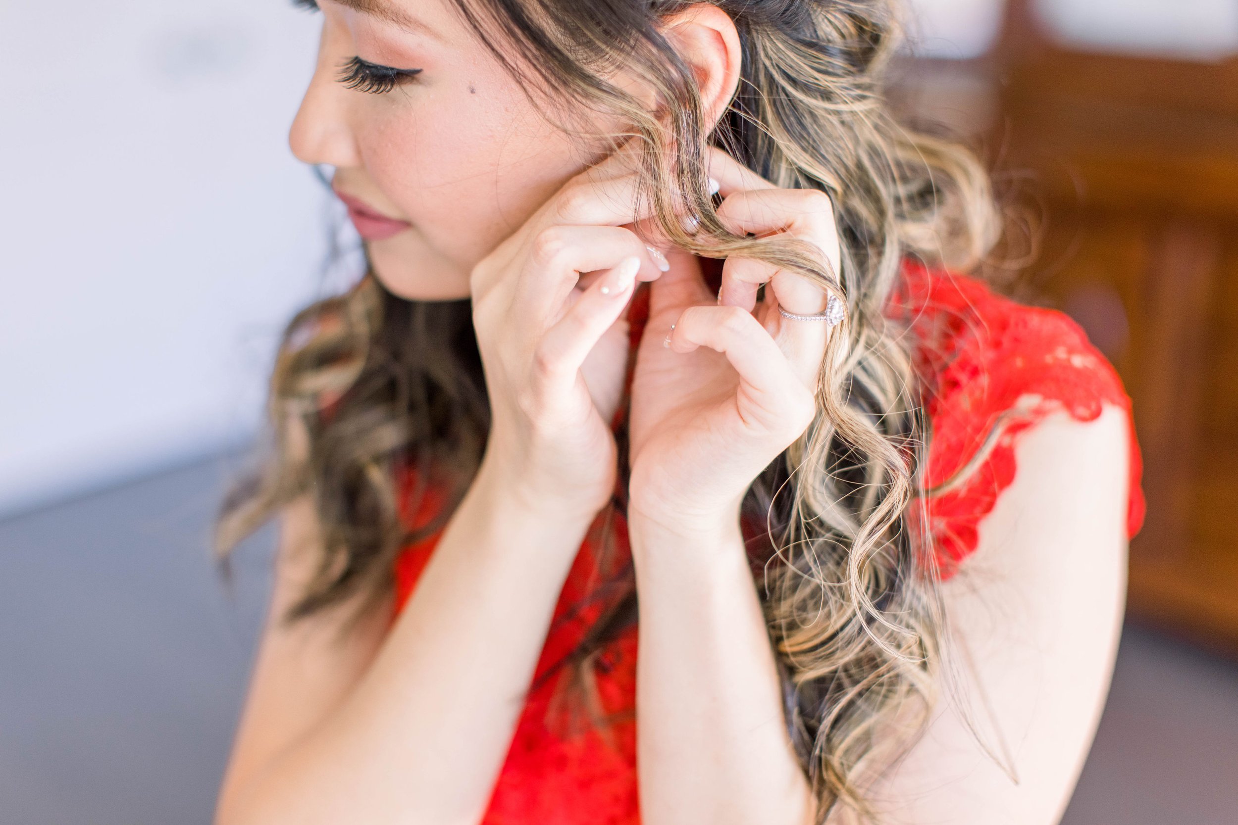  Bride putting in her earrings while wearing a red dress by Chelsea Mason Photography. red dress earrings wedding day #ChelseaMasonPhotography #ChelseaMasonWeddings #DowntownOttawa #FairmontChateauLaurier #OttawaWeddings #OttawaPhotographers 