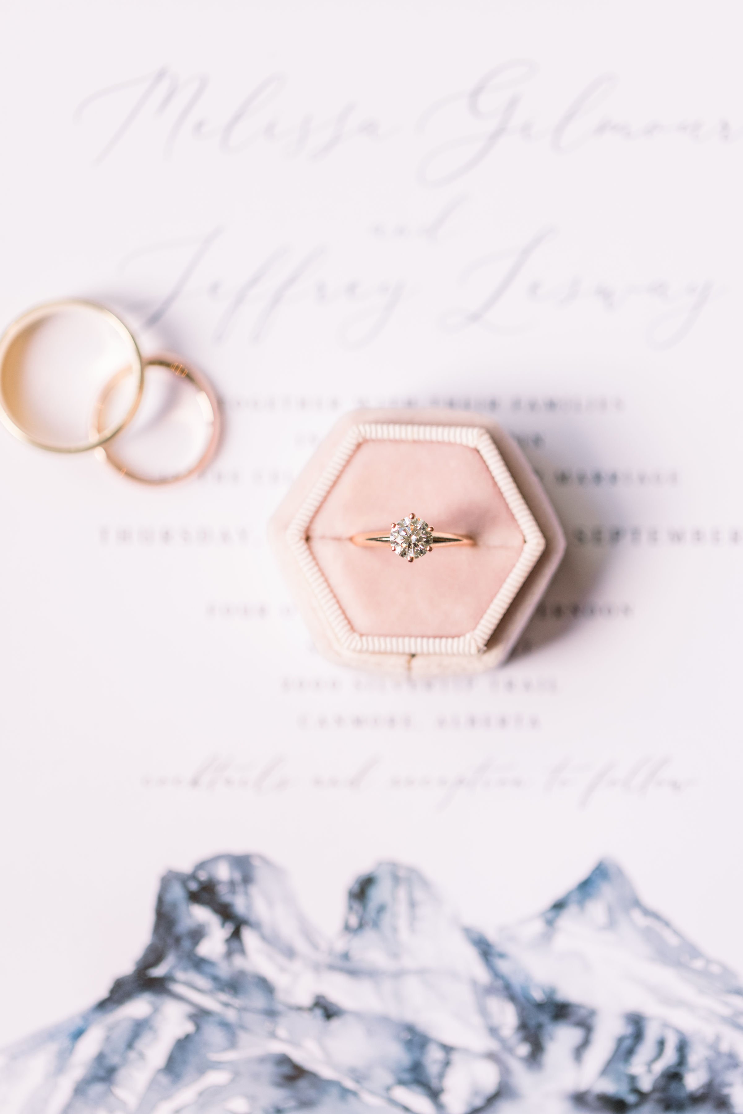  Flat-lay of a wedding ring in a pink box and wedding announcement with mountains by Chelsea Mason Photography. wedding ring #Albertaweddings #shesaidyes #Albertaweddingphotographers #SilvertipGolfCourse #ChelseaMasonPhotography #ChelseaMasonWeddings