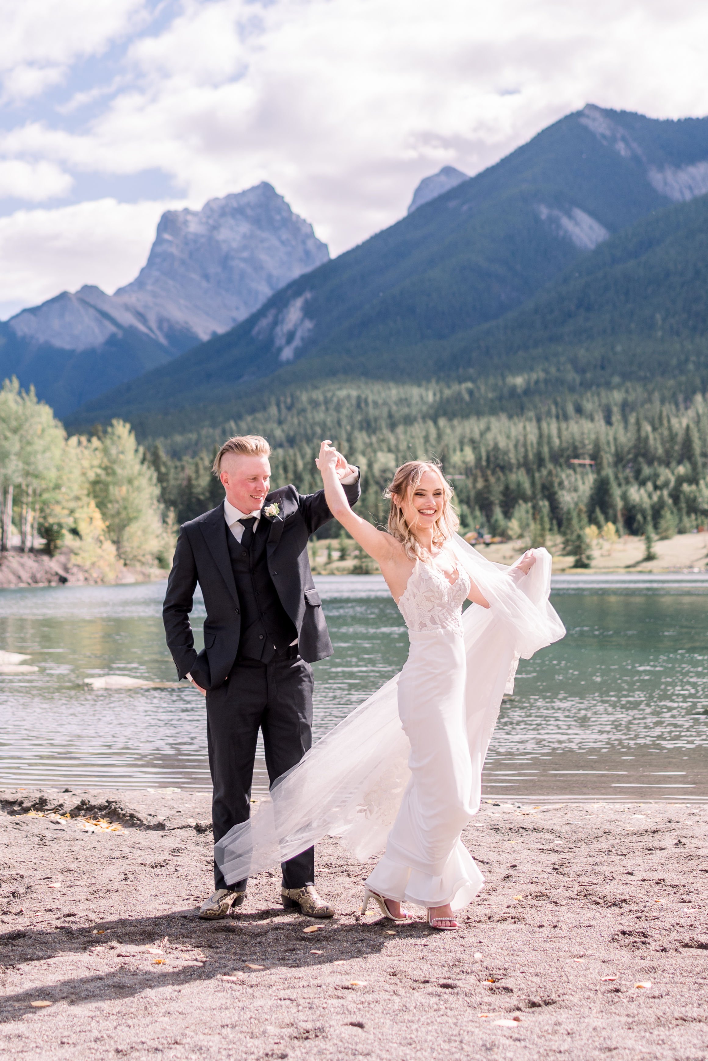  Next to a mountain lake, a groom twirls his bride captured by Chelsea Mason Photography. mountain lake wedding portraits #Albertaweddings #shesaidyes #Albertaweddingphotographers #SilvertipGolfCourse #ChelseaMasonPhotography #ChelseaMasonWeddings  
