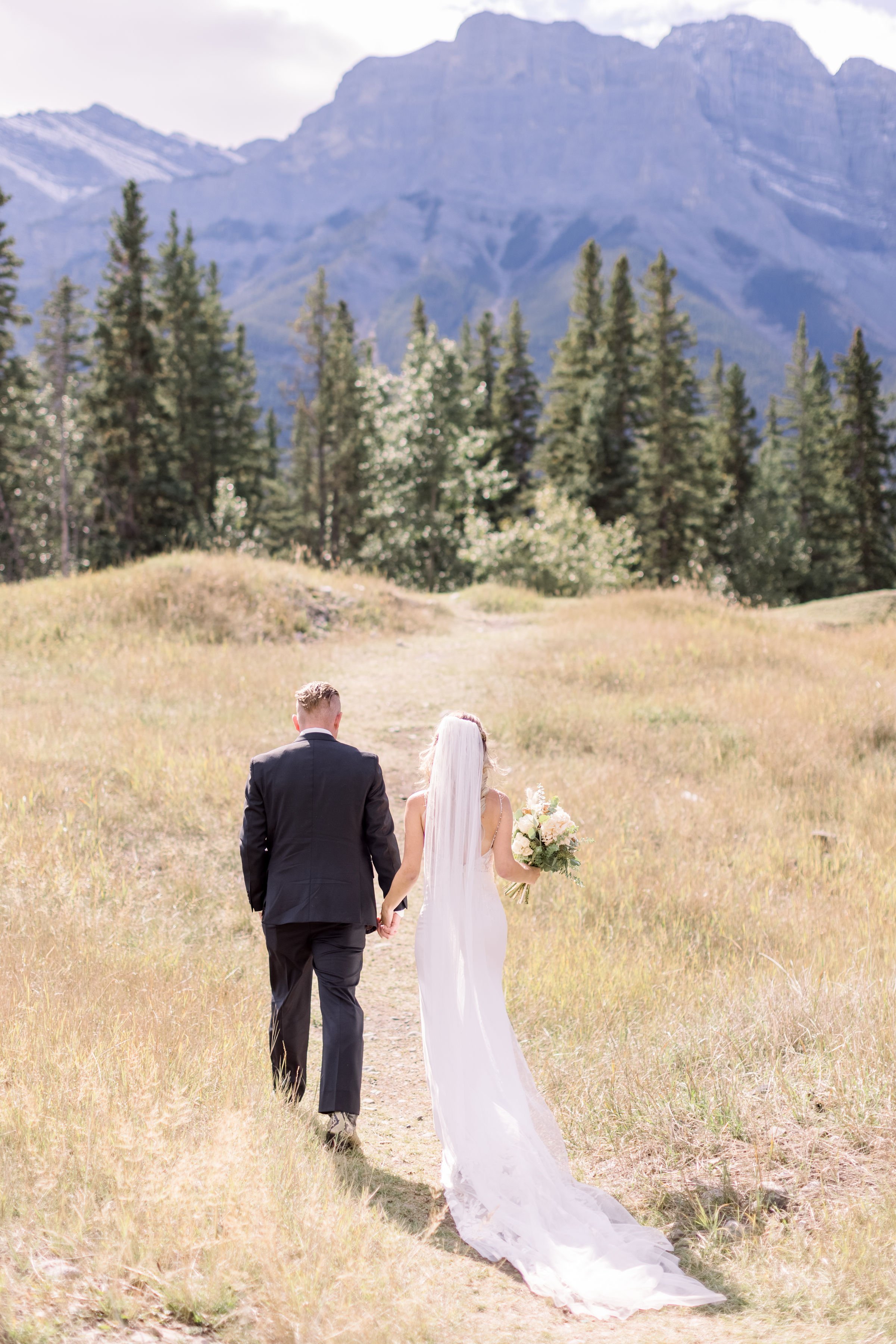  With blue mountains and yellow grass, a bride and groom walk around a mountainside by Chelsea Mason Photography. majestic wed #Albertawedding #shesaidyes #Albertaweddingphotographer #SilvertipGolfCourse #ChelseaMasonPhotography #ChelseaMasonWeddings