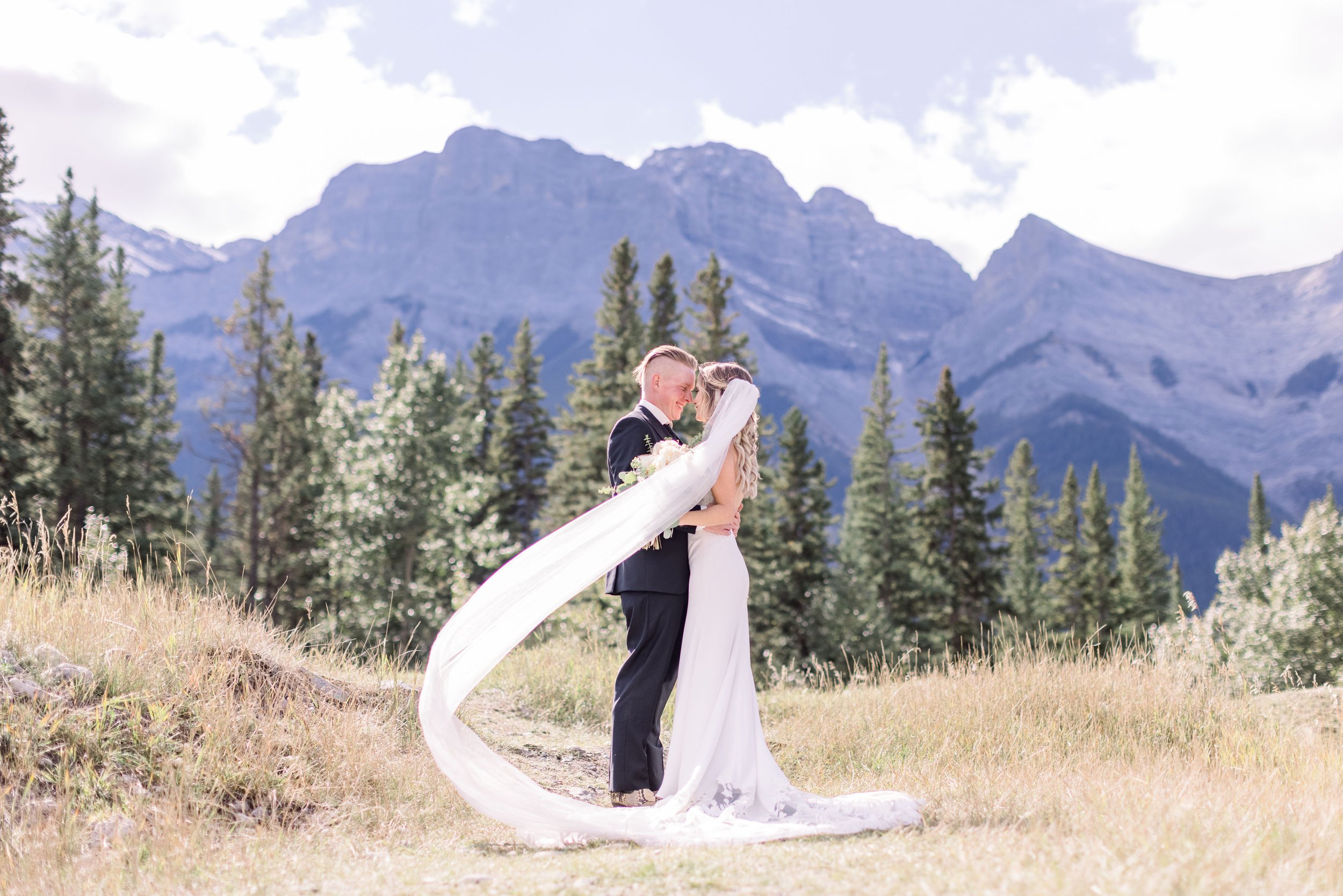  Under the Banff mountains, a bride's veil blows in the wind while kissing her groom by Chelsea Mason Photography. veil Banff #Albertaweddings #shesaidyes #Albertaweddingphotographer #SilvertipGolfCourse #ChelseaMasonPhotography #ChelseaMasonWeddings