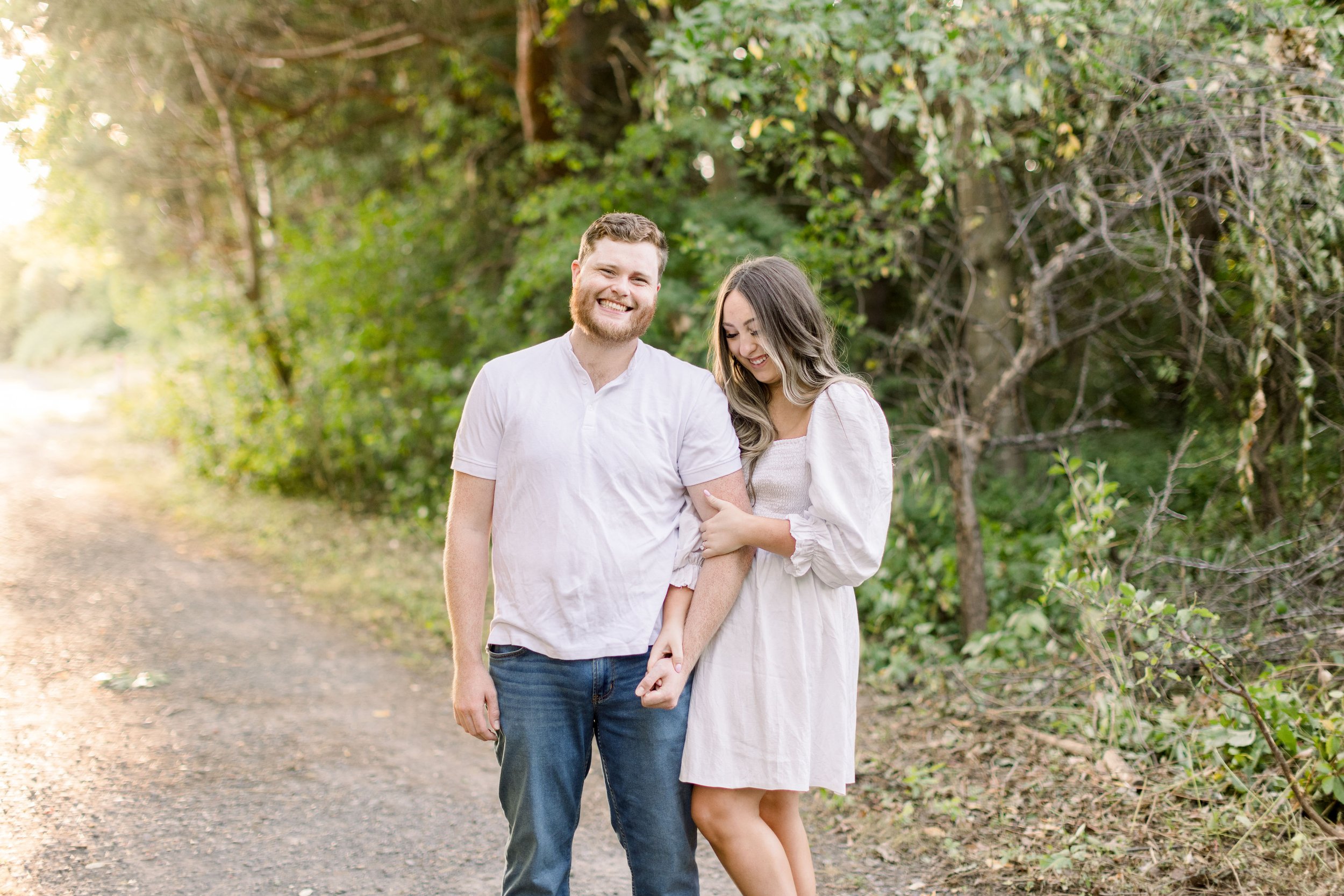  At the Ottawa Arboretum in golden sunlight, an engaged couple smiles for a portrait by Chelsea Mason Photography. outdoor #ChelseaMasonPhotography #ChelseaMasonEngagements #Ottawaphotographers #ArboretumOttawaEngagments #weddingannouncementportraits