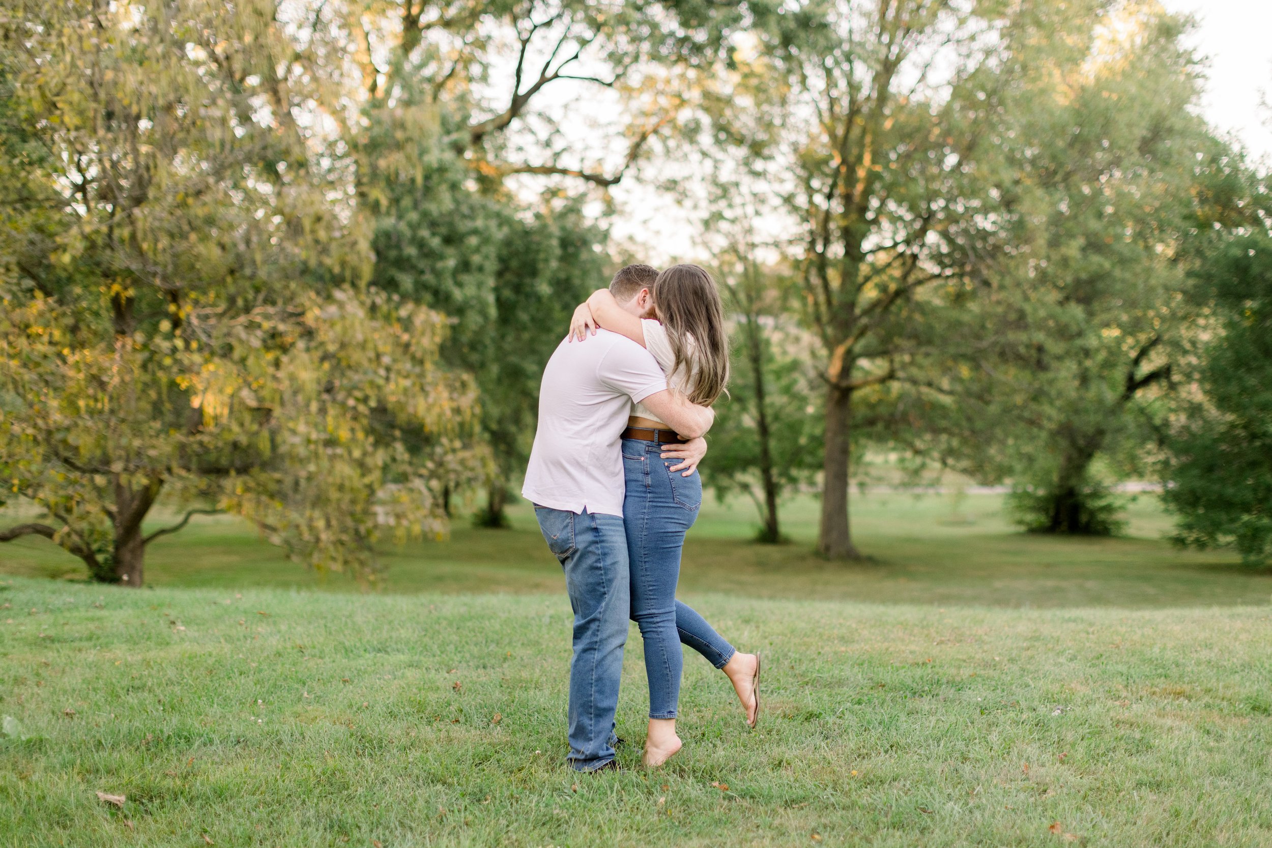  With shoes off an engaged couple embraces on a green grass field by Chelsea Mason Photography. summer engagement #ChelseaMasonPhotography #ChelseaMasonEngagements #Ottawaphotographers #ArboretumOttawaEngagments #weddingannouncementportraits 