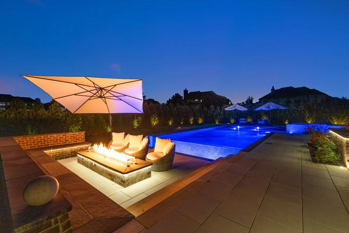 Gas-fueled fire pit and L-shaped bench seating beside an infinity edge pool