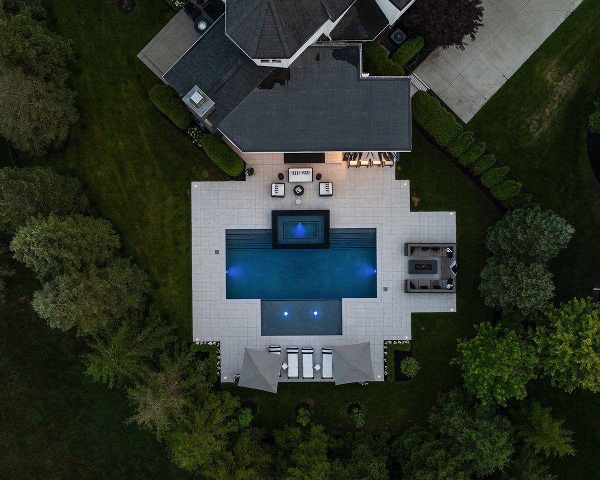 contemporary outdoor entertainment space in Rochester Hills Michigan with porcelain tile patio surrounding a custom gunite pool and spa