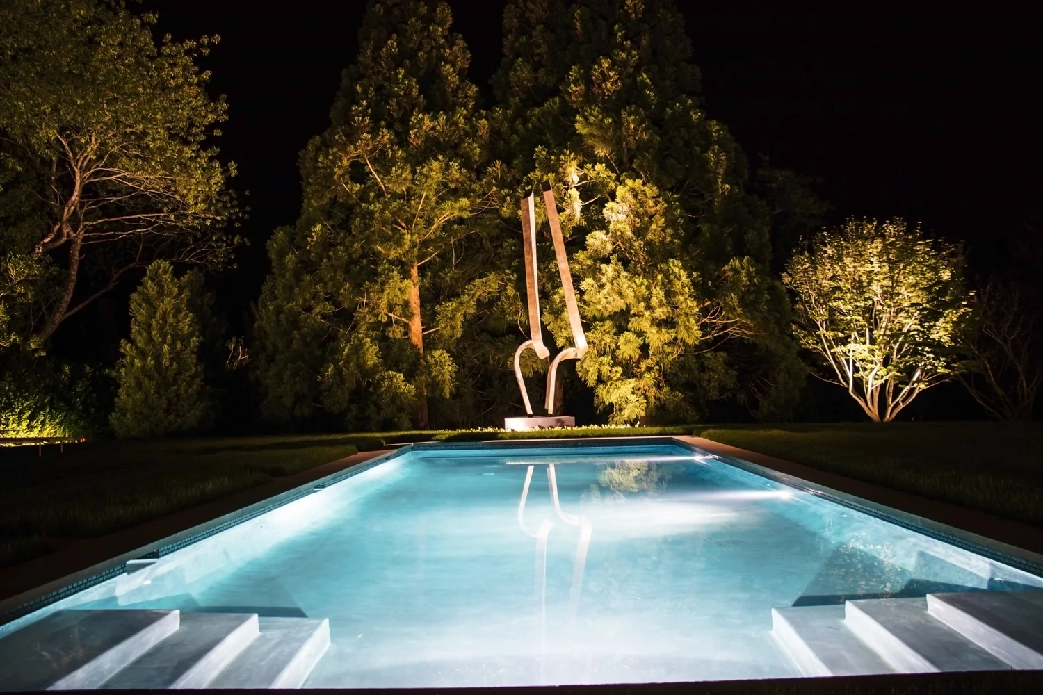 Pool area lighting at Watermill estate — atmospheric poolside landscape lighting at night