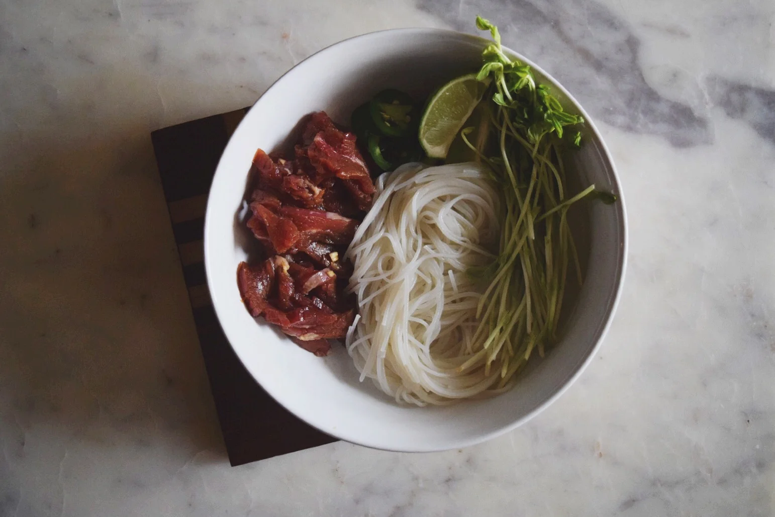 bowl with accoutraments and raw beef, ready to be filled with broth.