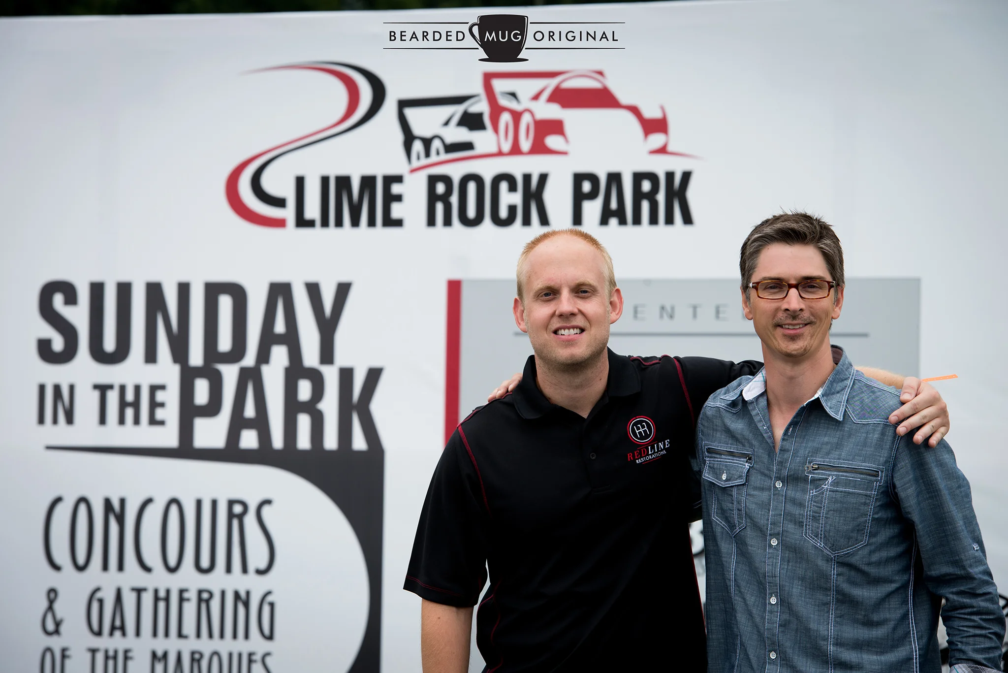 PJ from Redline Restorations and Dwight from The Little Red Racing Car pose in front of the official backdrop.