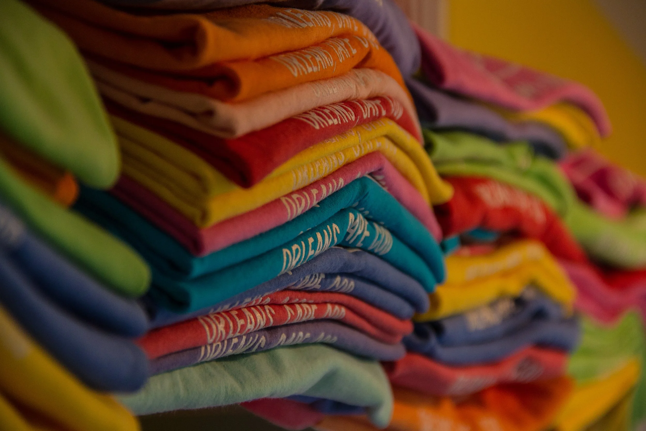 Stacked colorful fabric or clothing items, folded and arranged in layers, in various bright colors like orange, red, yellow, pink, blue, and green.