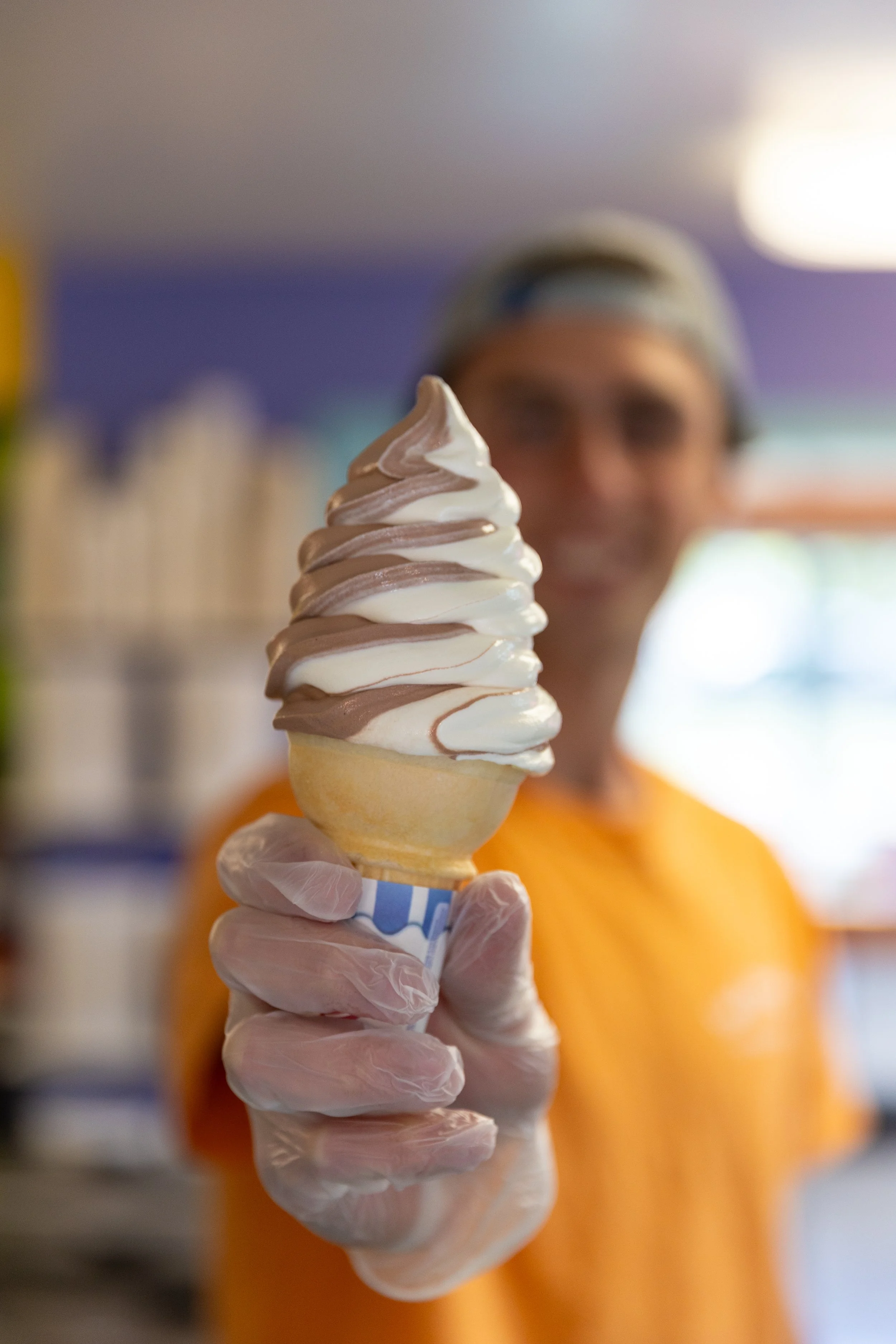 A vanilla soft serve ice cream cone in a waffle cone with a swirl on top, against a light blue background.