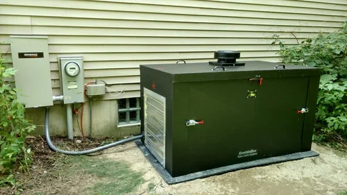 A large rectangular generator enclosure sits on a concrete pad beside beige siding and electrical boxes.