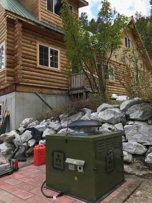 A green power generator unit sitting on a brick patio near large rocks and a multi-story log cabin exterior.