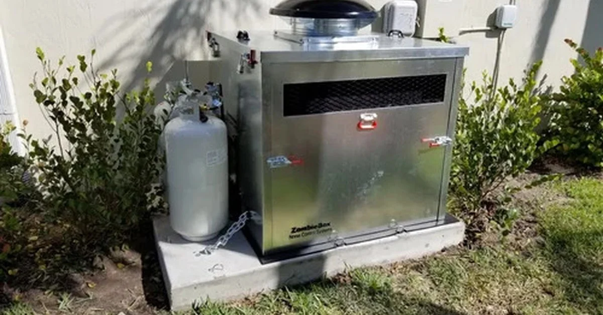 A metal generator enclosure sits on a concrete pad beside a wall, gas cylinder, shrubs, and utility boxes.
