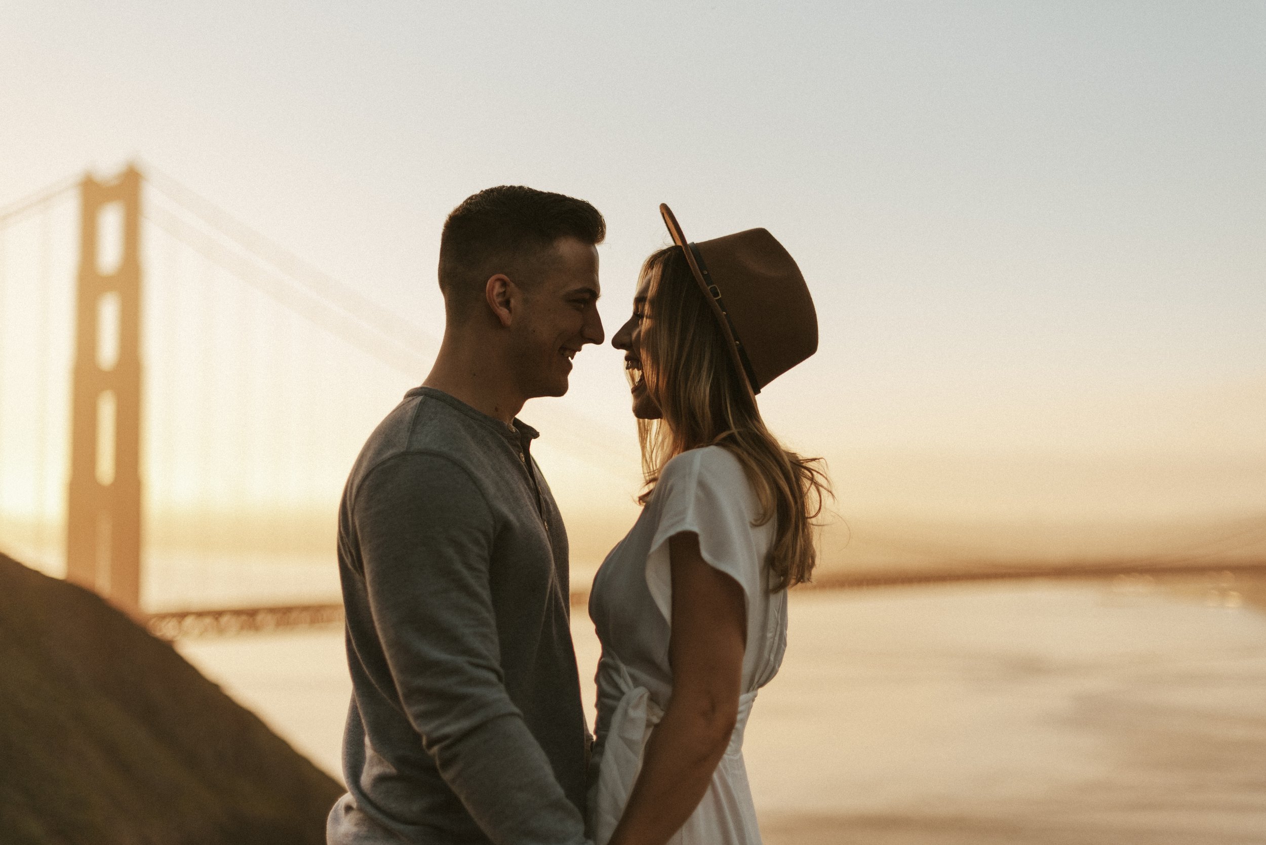 Couple standing closely in front of Golden Gate Bridge.