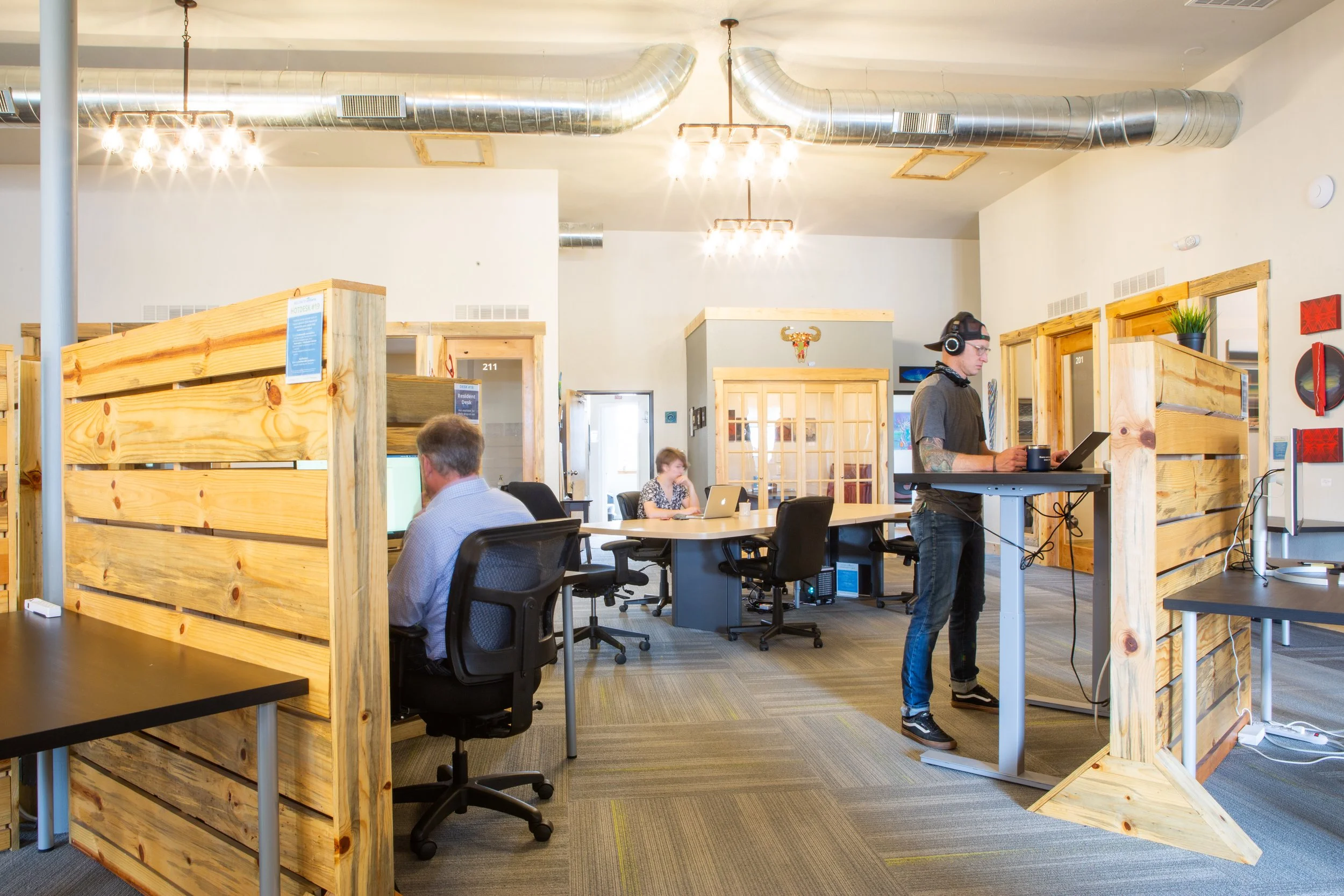 Coworking space with wooden desk dividers, people working at seated and standing desks.