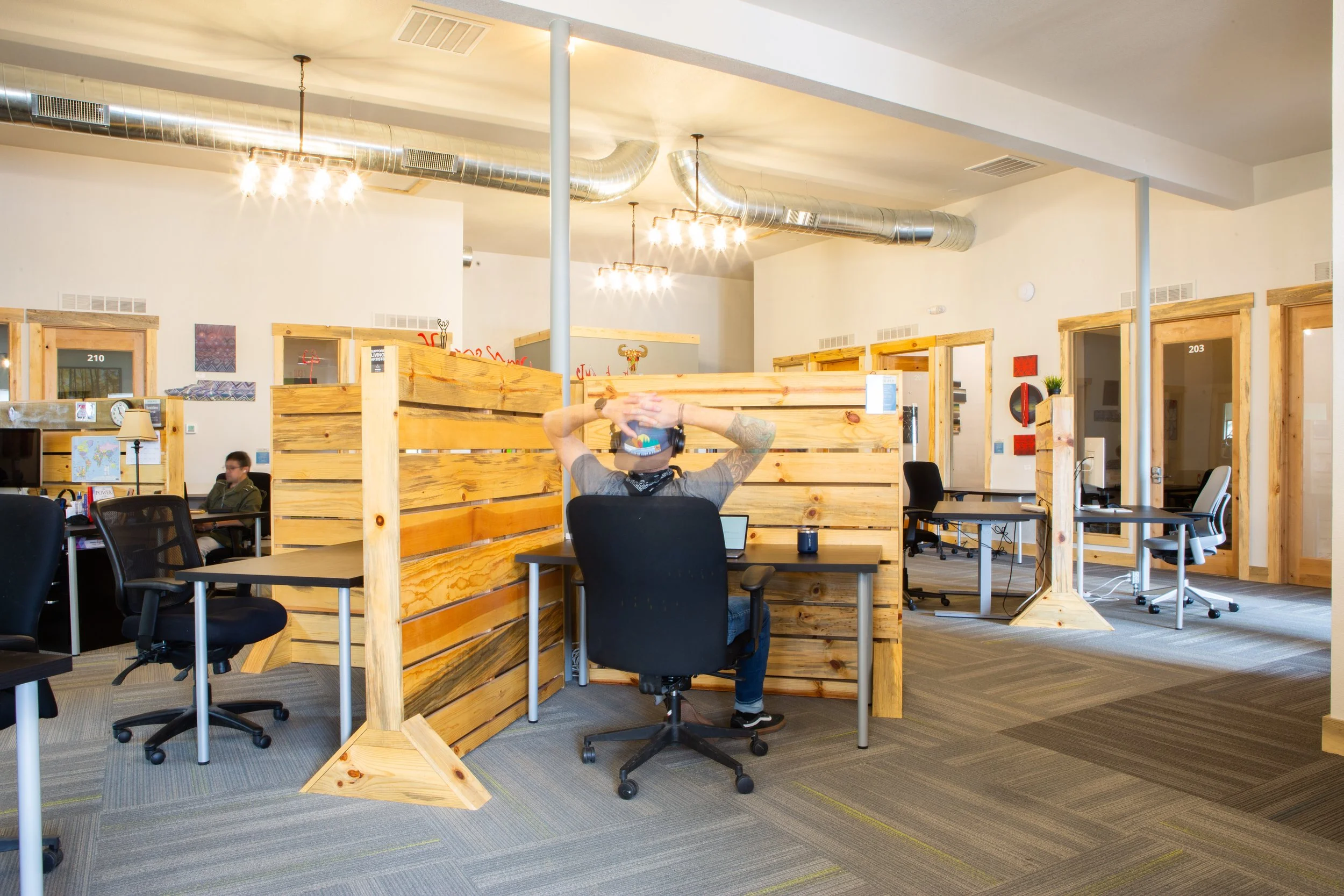 Man working at a wooden partitioned desk in an open coworking space.