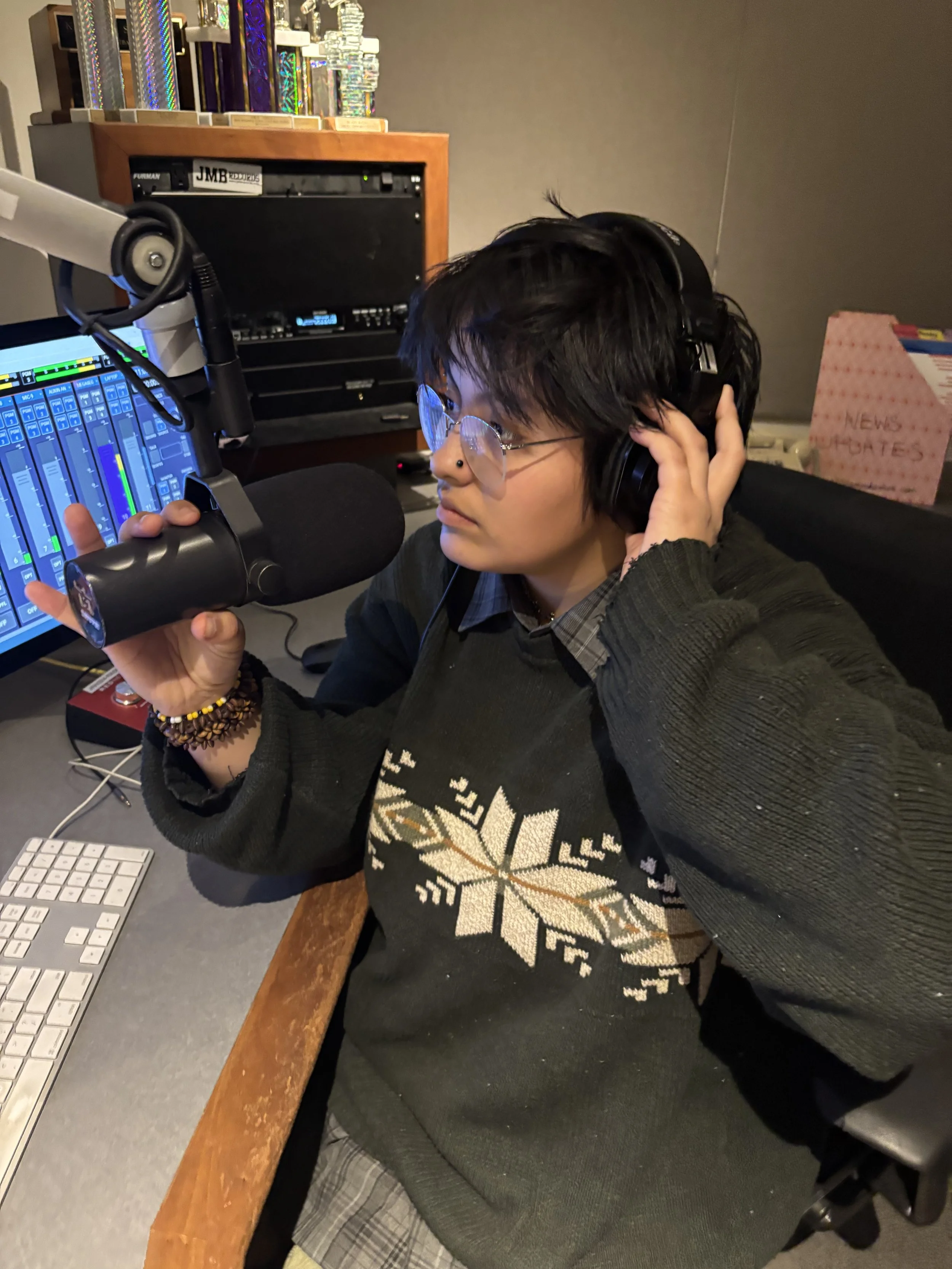 Photo of Gib Manrique in a black sweatshirt speaking into a podcast microphone.