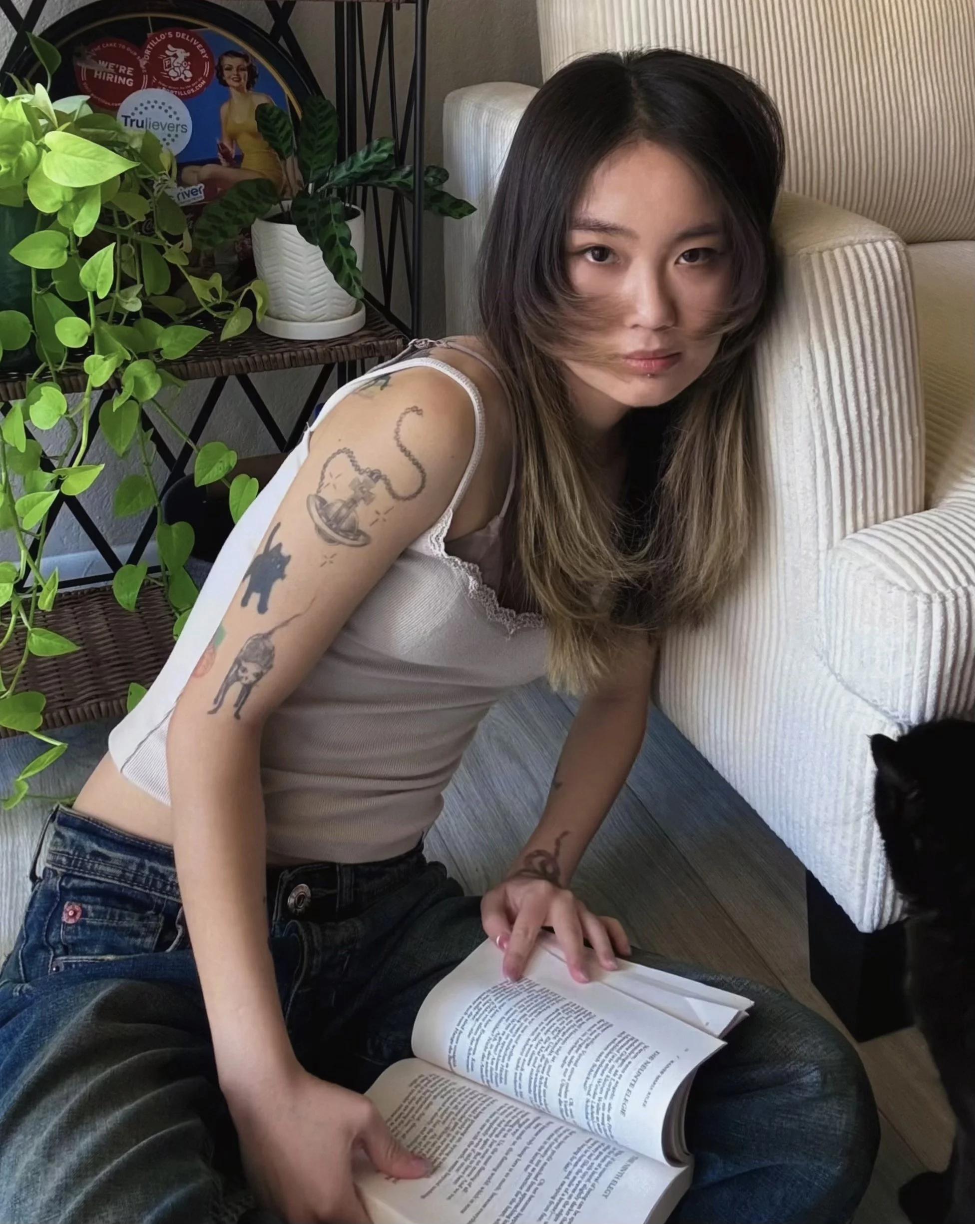 Photo of Tsong Chang in white tank top with open book in lap and leaning against a cream-colored couch.